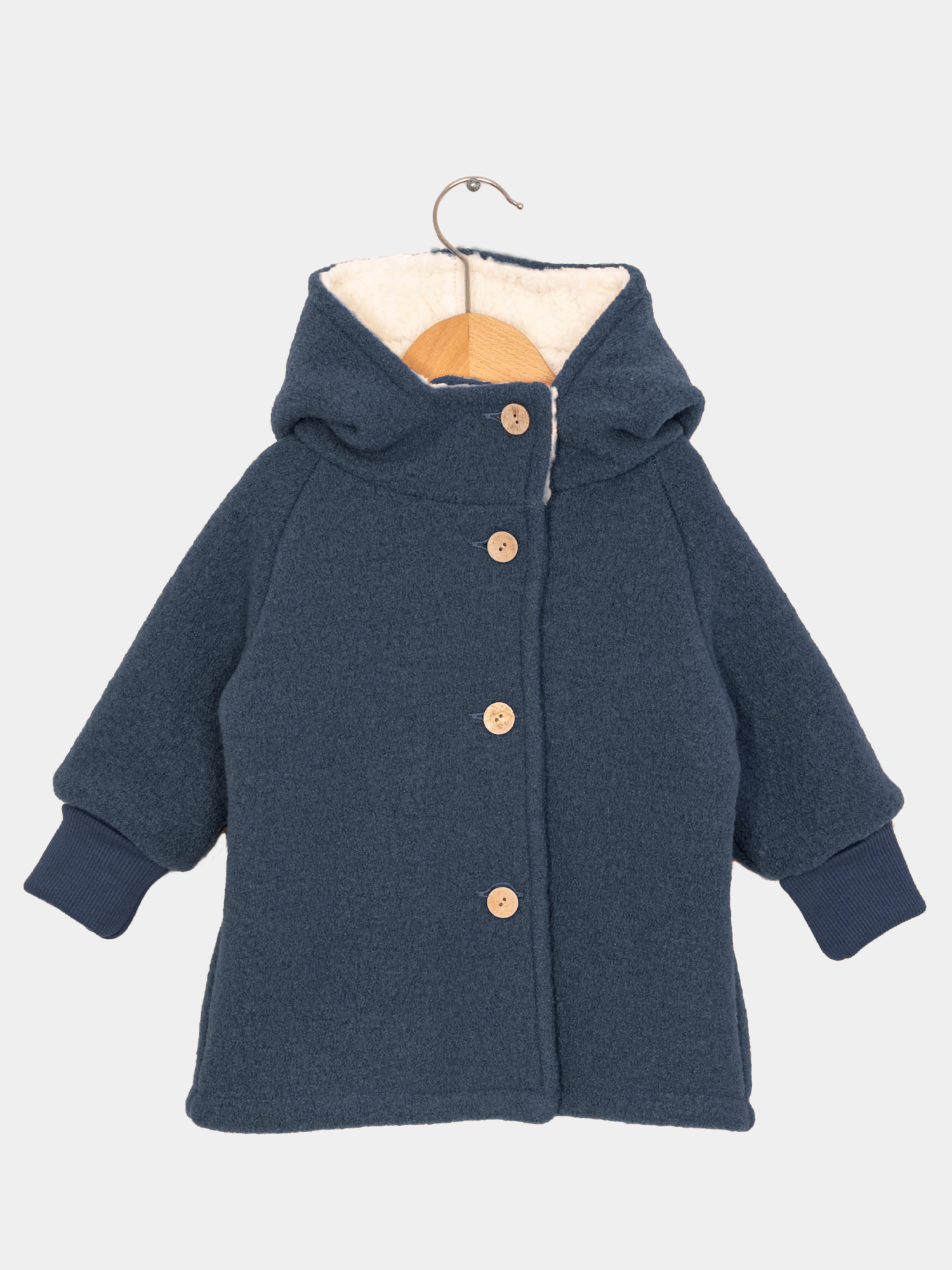Teddy-Wichteljacke Wollwalk - Marine: Dunkelblaue Kinderjacke mit spitzer Kapuze, sichtbarem Teddyfutter in der Kapuze, Holzknöpfen und langen Ärmeln mit gerippten Bündchen, auf einem Holzkleiderbügel hängend.