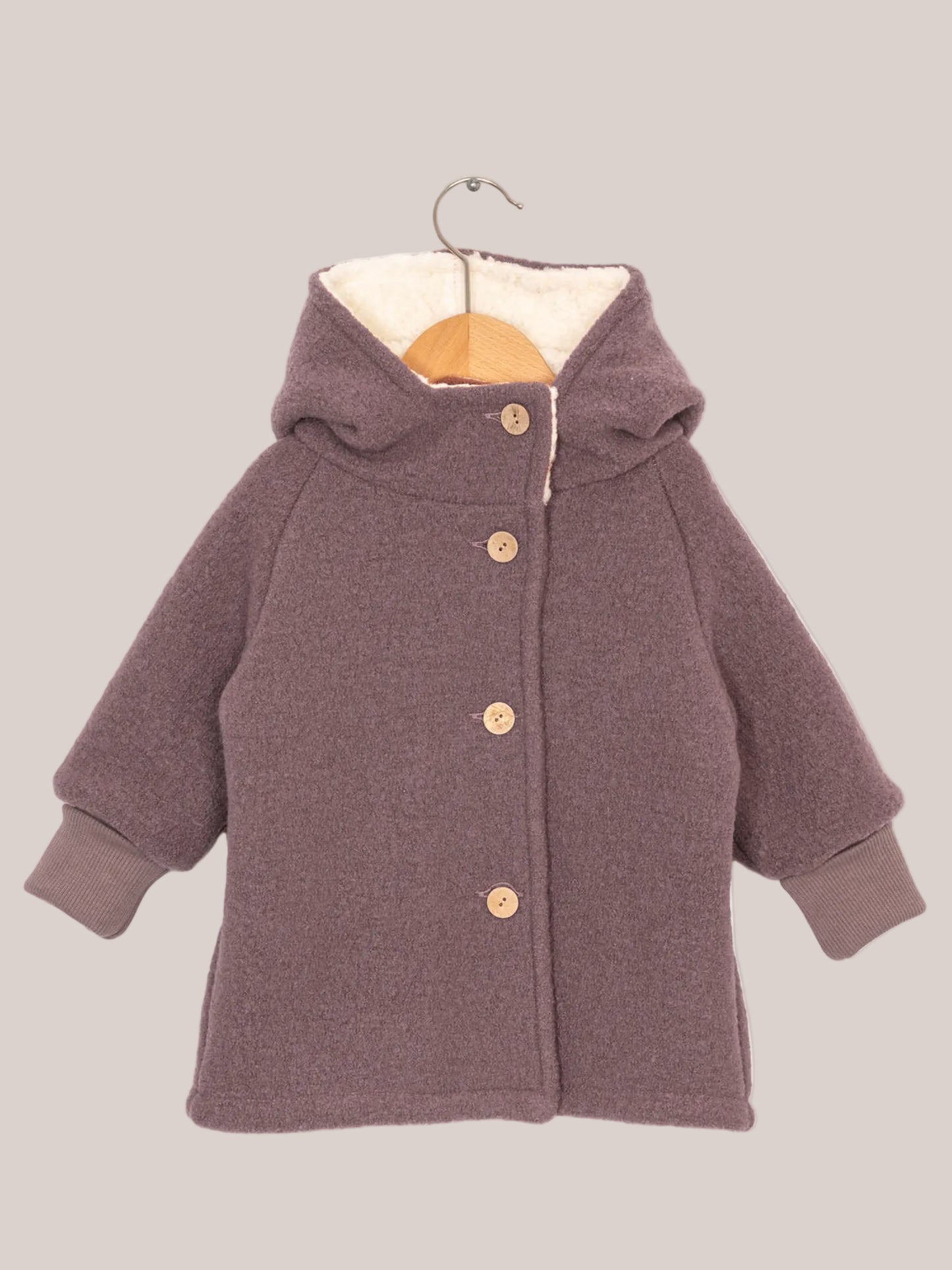 Teddy-Wichteljacke Wollwalk - Malve auf einem Haken hängend, zeigt Details wie gestrickte Ärmel und Knöpfe, ideal für kalte Wintertage dank Teddyfutter.
Wollwalkjacke und Winterjacke für Kinder. Handgenäht in Berlin