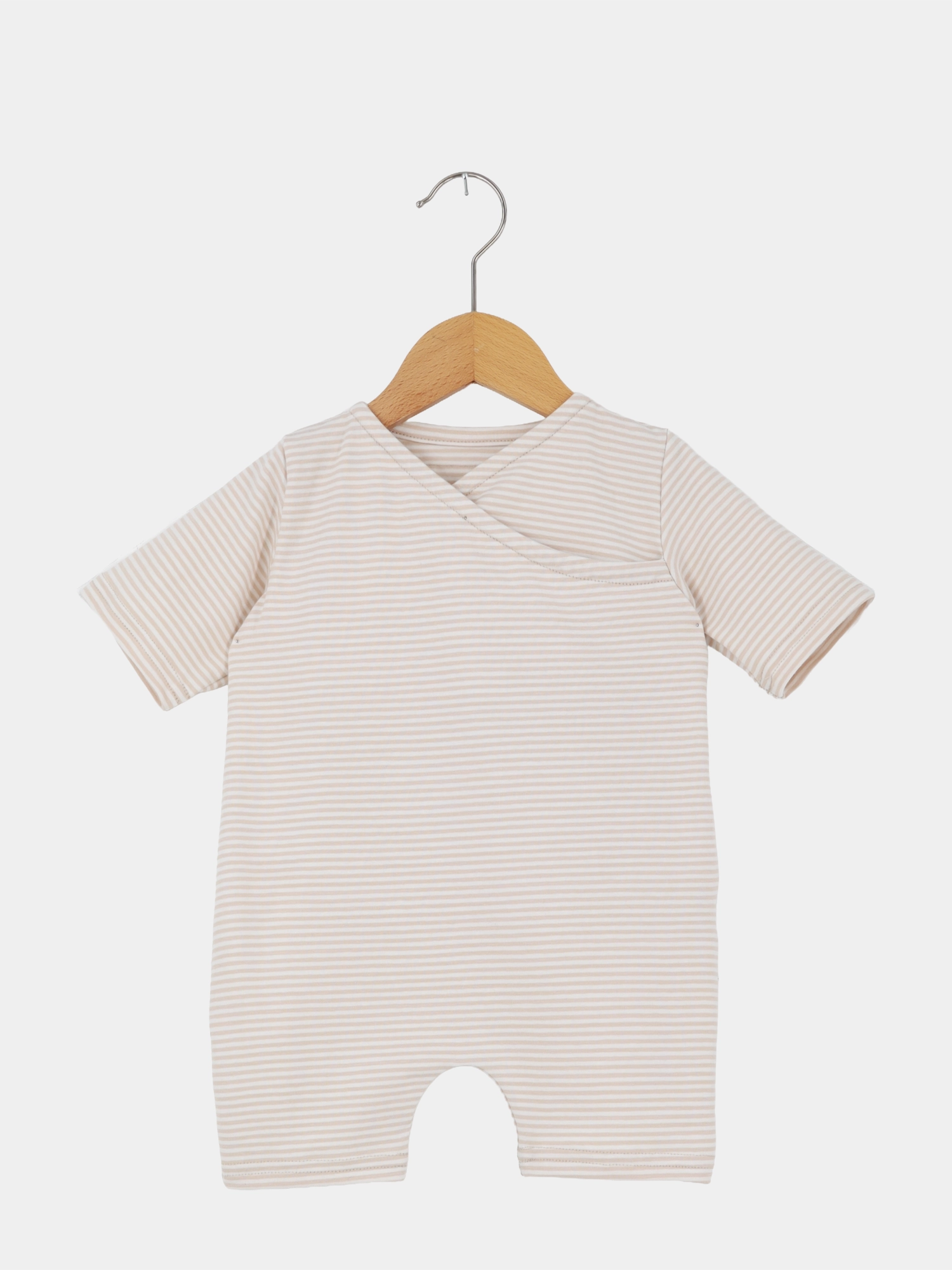 Wickel Overall Baumwolle - Sand: Kurzärmeliger Baby-Overall aus weichem, gestreiftem Stoff mit Kimono-Ausschnitt und Beinbogen-Details, auf einem Holzkleiderbügel hängend.