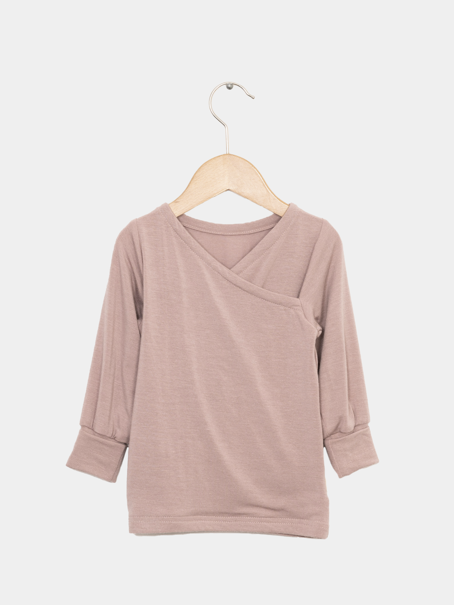 Wickelshirt aus Kaschmir-Mix - Puder, präsentiert auf einem Kleiderbügel. Der elegante Schnitt unterstreicht die hochwertige Verarbeitung, ideal als vielseitiges Oberteil oder Unterhemd für Kinder.