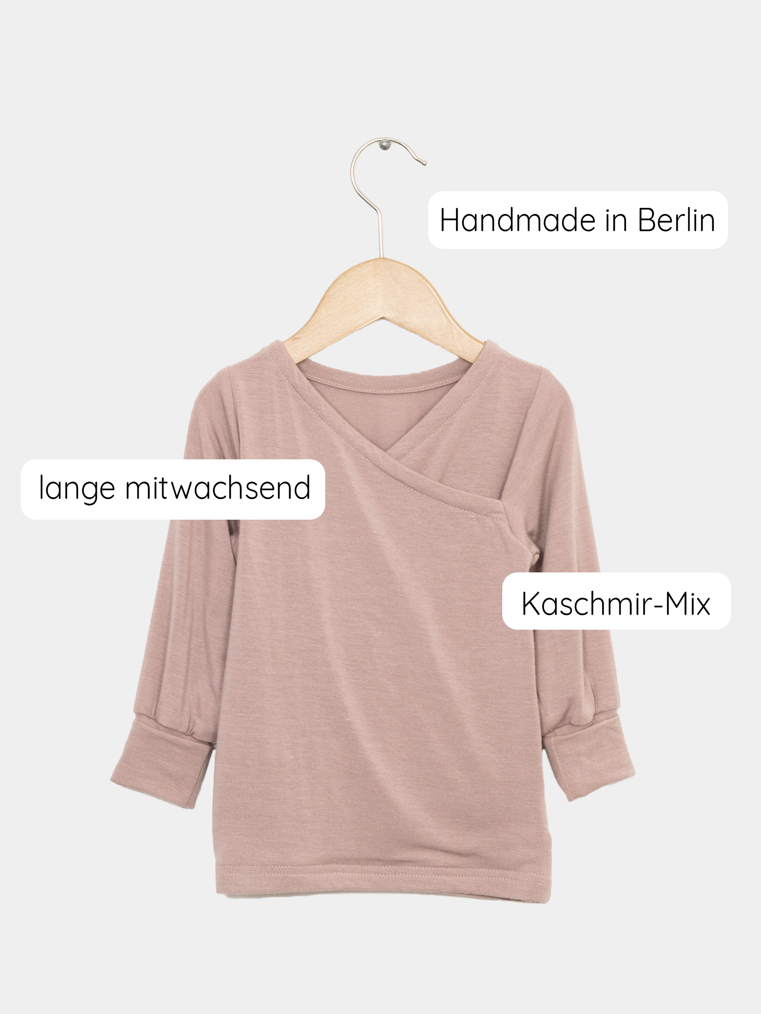 Wickelshirt aus Kaschmir-Mix - Puder: Ein weich anmutendes Wickelshirt, drapiert auf einer Schaukel, zeigt sein elastisches, hochwertiges Material, ideal als Shirt oder Unterhemd für Kinder.