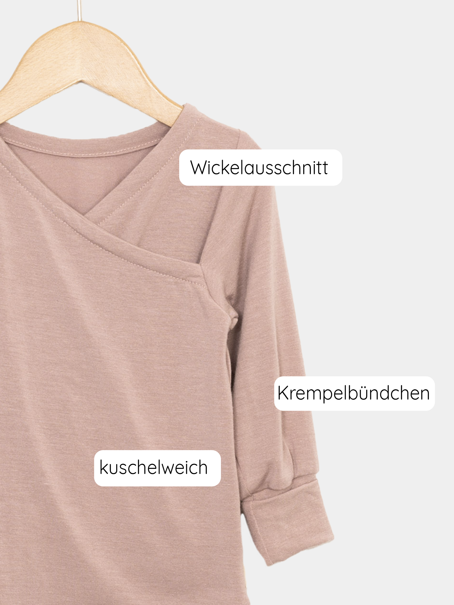 Das Wickelshirt aus Kaschmir-Mix - Puder zeigt eine Nahaufnahme eines kuschelweichen Shirts mit einem dezenten Logo, das ideal als Shirt oder Unterhemd für Kinder getragen werden kann.