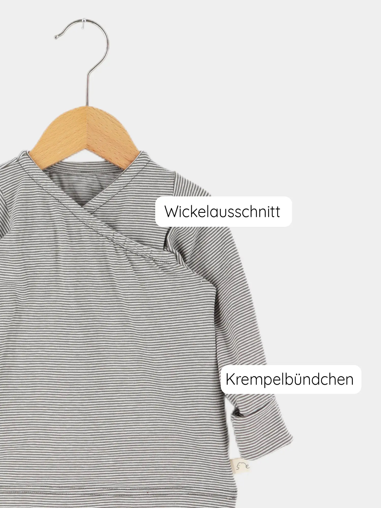 Das Wickelshirt aus Bio-Baumwolle - Ringel Maus zeigt ein gestreiftes Baby-Langarmshirt auf einem Holzbügel mit Wickelausschnitt und krempelbaren Bündchen, ideal für einfaches Anziehen und Mitwachsen.