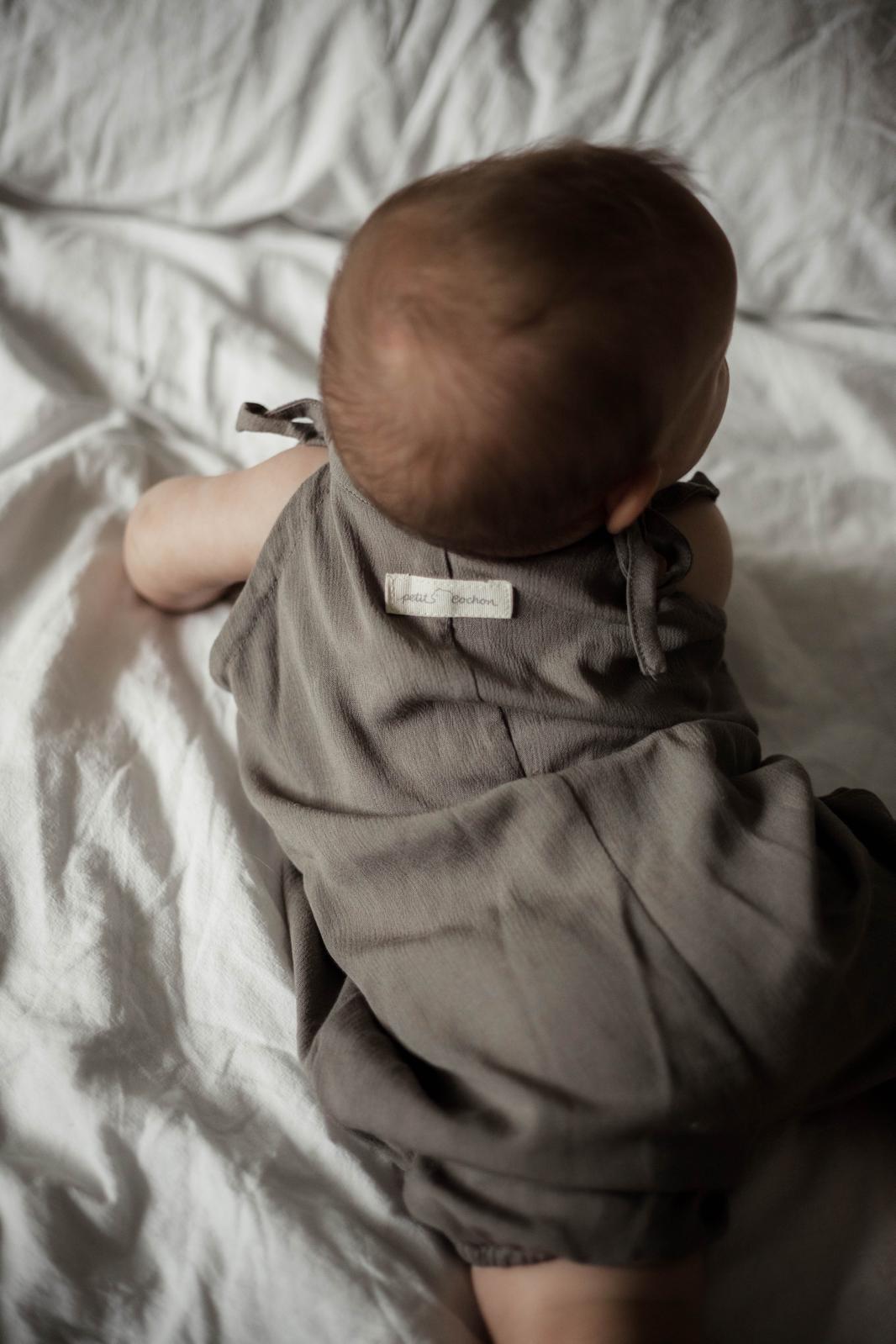 Kurze Latzhose zum Binden Viskose Maus Gr 6M: Ein Baby liegt auf einem Bett. Nahe Ansicht von Babyhaar und einem unscharfen Ohr, die die Latzhose in einer gemütlichen Umgebung präsentieren.
