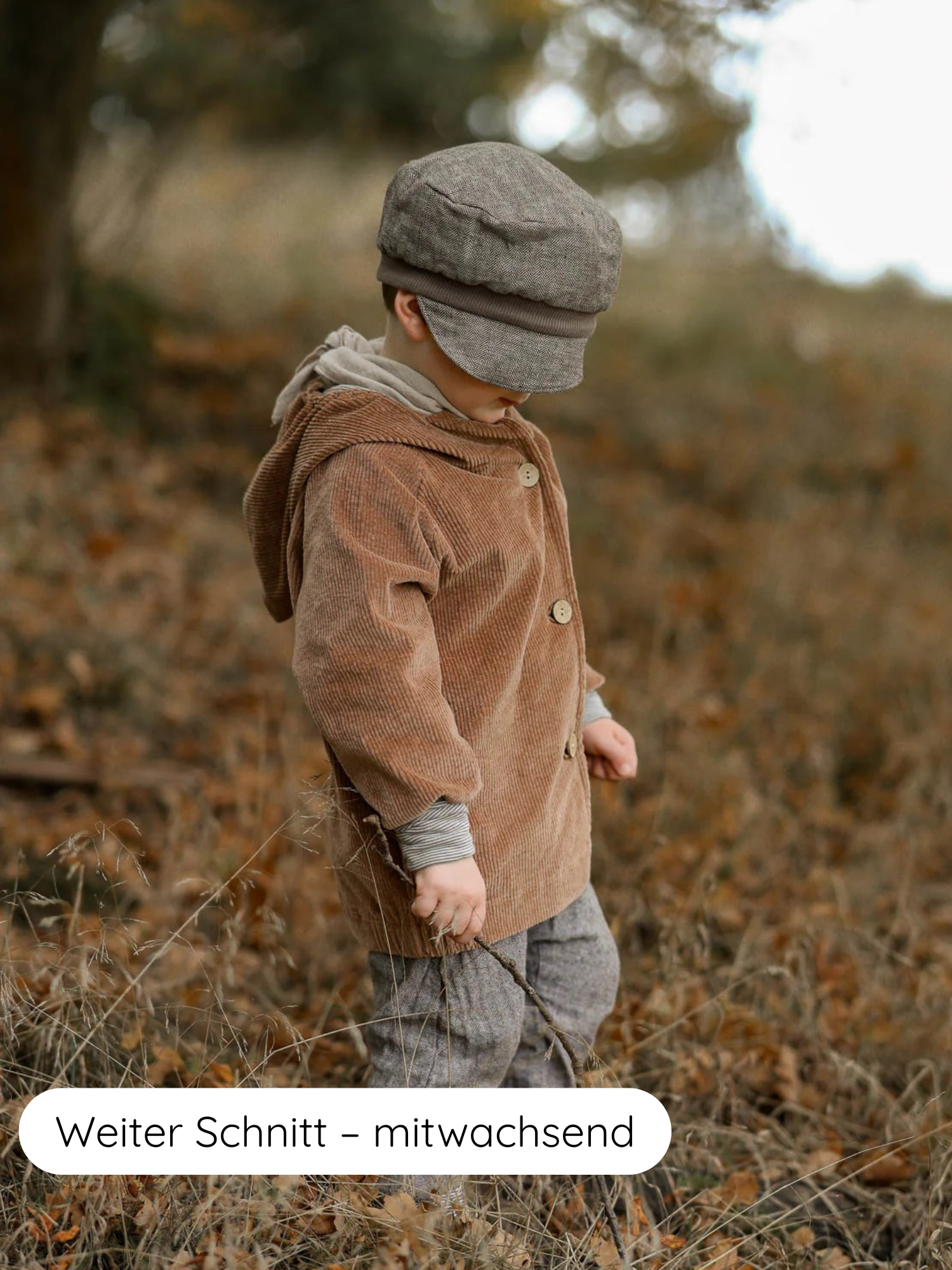 Ein Kind trägt die Wichteljacke Breitcord Stretch - Weizen mit großen Holzknöpfen und krempelbaren Ringel-Armbündchen, während es in einem Herbstfeld steht. Ein graues Tweed-Outfit ergänzt den Look.