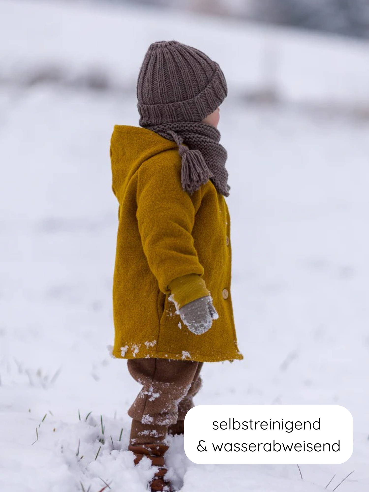 Kind im Profil im Schnee mit Wichteljacke Wollwalk - Honig. Die Jacke ist wasserabweisend, selbstreinigend und ideal für kalte Jahreszeiten. Kombiniert mit grauen Accessoires und braunen Hosen.