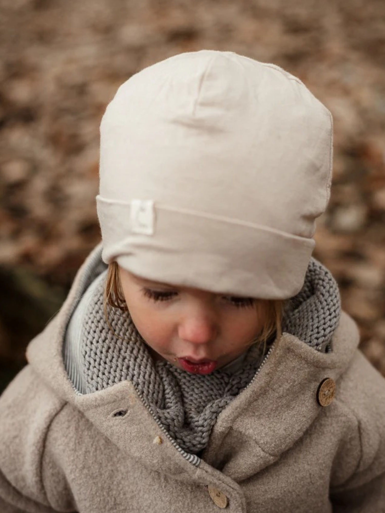 Ein Kleinkind trägt die Wichteljacke Wollwalk - Sand mit Holzknöpfen, passt perfekt für kühleres Wetter. Unter der Jacke ist ein grauer Strick sichtbar, ideal für Herbst und Winter.