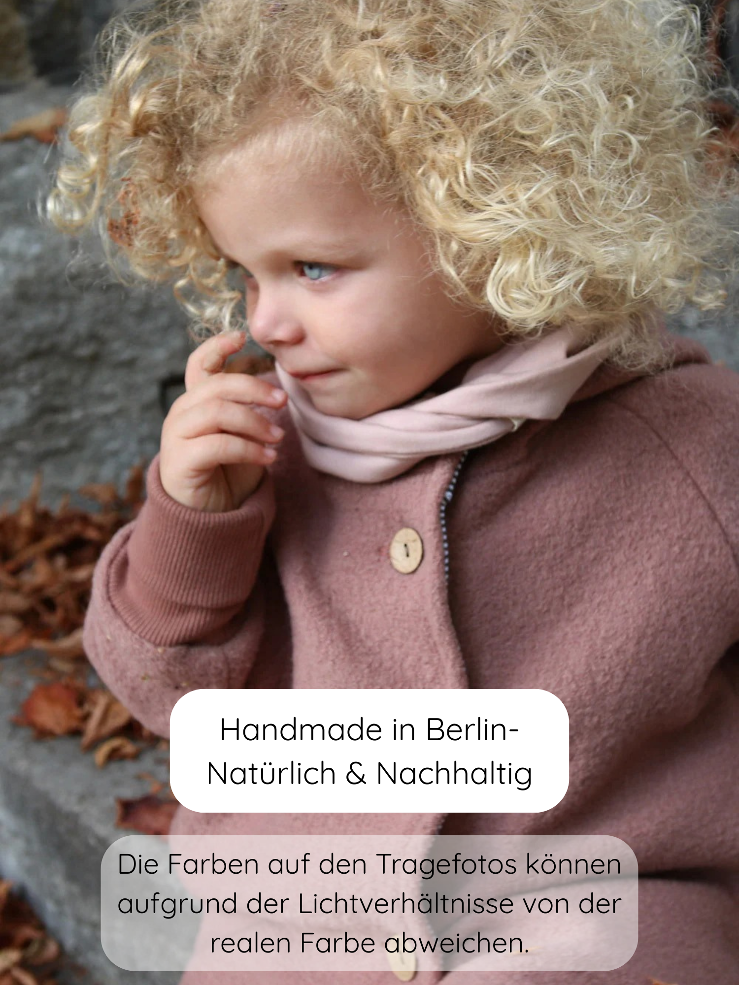 Ein Kleinkind trägt die Wichteljacke Wollwalk - Zimt mit Holzknöpfen und Bio-Jersey-Futter, sitzt auf Laub bedeckten Steintreppen, was die Vielseitigkeit und hochwertige Verarbeitung der Jacke unterstreicht.