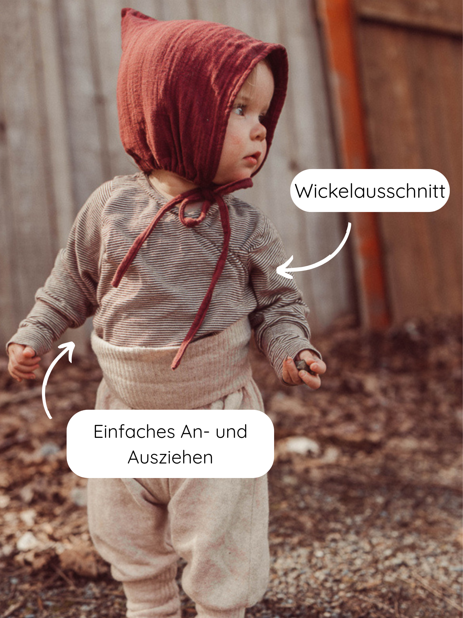 Kleinkind in Wickelshirt aus Bio-Baumwolle - Ringel Schoko mit Wickelschnitt, weichem Stoff und krempelbaren Bündchen, kombiniert mit hochgeschnittener Hose und schlichter Mütze, auf einem herbstlichen Boden stehend.