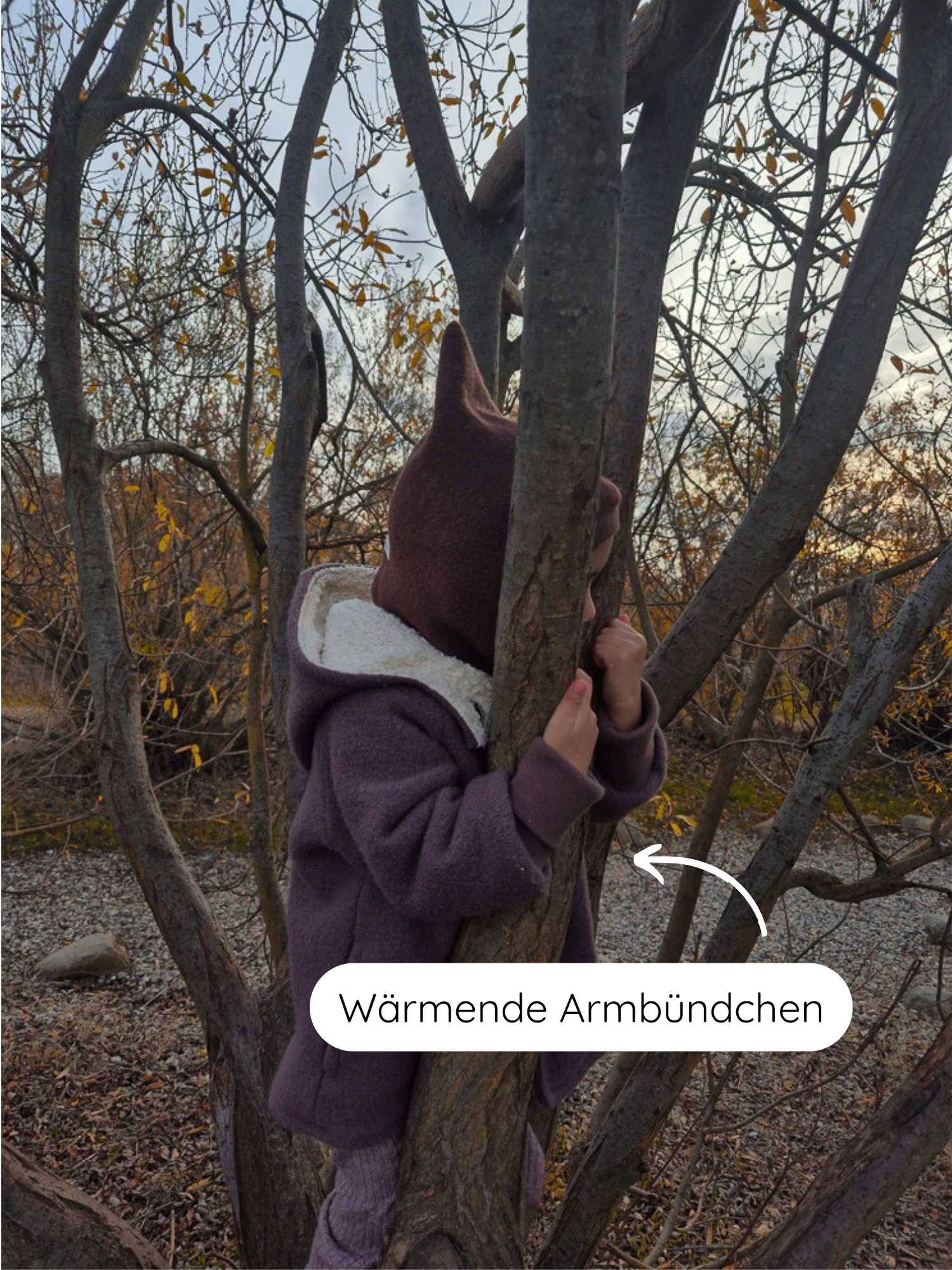 Kleinkind in einer Baumkrone trägt die Winter Wichteljacke Wollwalk mit Teddyfutter - Malve, mit spitzer Kapuze und wärmenden Armbündchen, betont durch einen deutschen Hinweis auf die Ärmel.