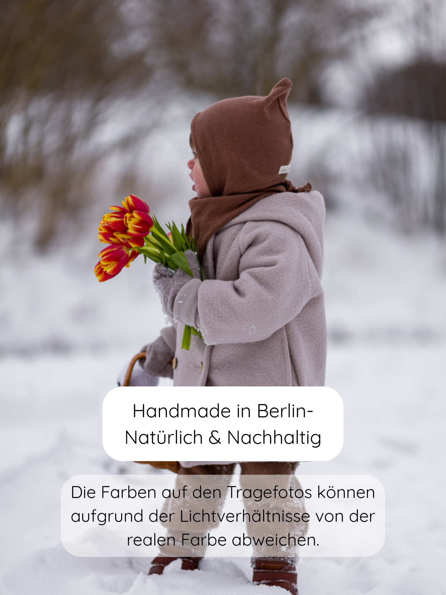 Kind steht im Schnee, trägt die Zwergenmütze Strick - Nougat aus recycelter Baumwolle, kombiniert mit grauem Mantel und hält Tulpenstrauß; handgefertigt in Berlin für umweltfreundliche Wärme.