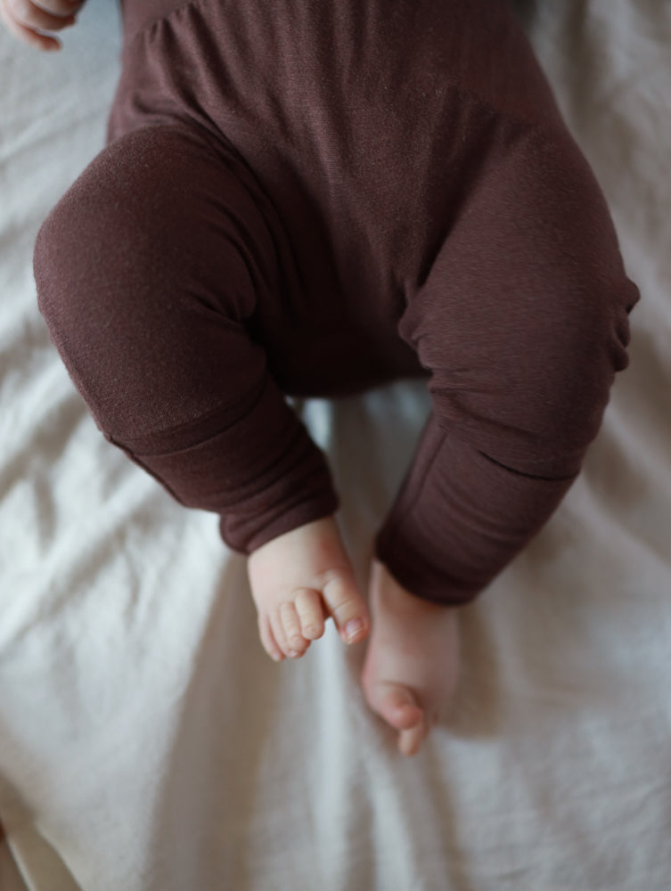 Babyknicker Bambusviskose Zartbitter, getragen von einem Säugling, zeigt weiche, atmungsaktive braune Leggings, die sanft die Babyhaut umschmeicheln und Bewegungsfreiheit für Strampeln und Entdecken bieten.