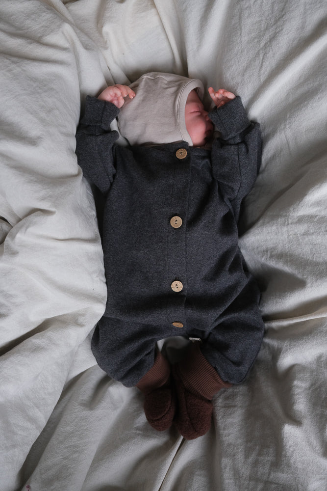 Neugeborenes in einem grauen Einteiler mit Babybooties Wollwalk - Schoko aus gewalkter Schurwolle, die Wärme speichern. Die Booties haben elastische Bündchen und passen gut zu Wollwalkanzügen.
