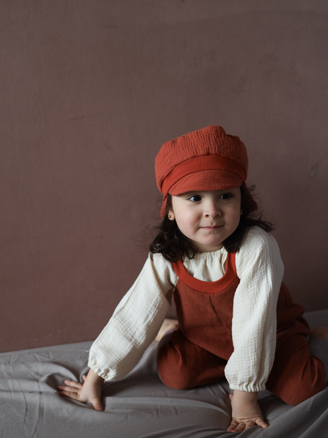 Ein Kleinkind trägt die Michelmütze Bio-Musselin mit Nackenschutz - Terrakotta. Die Mütze sitzt bequem dank elastischem Bündchen und schützt vor Sonne. Ideal aus nachhaltigem Bio-Musselin gefertigt.