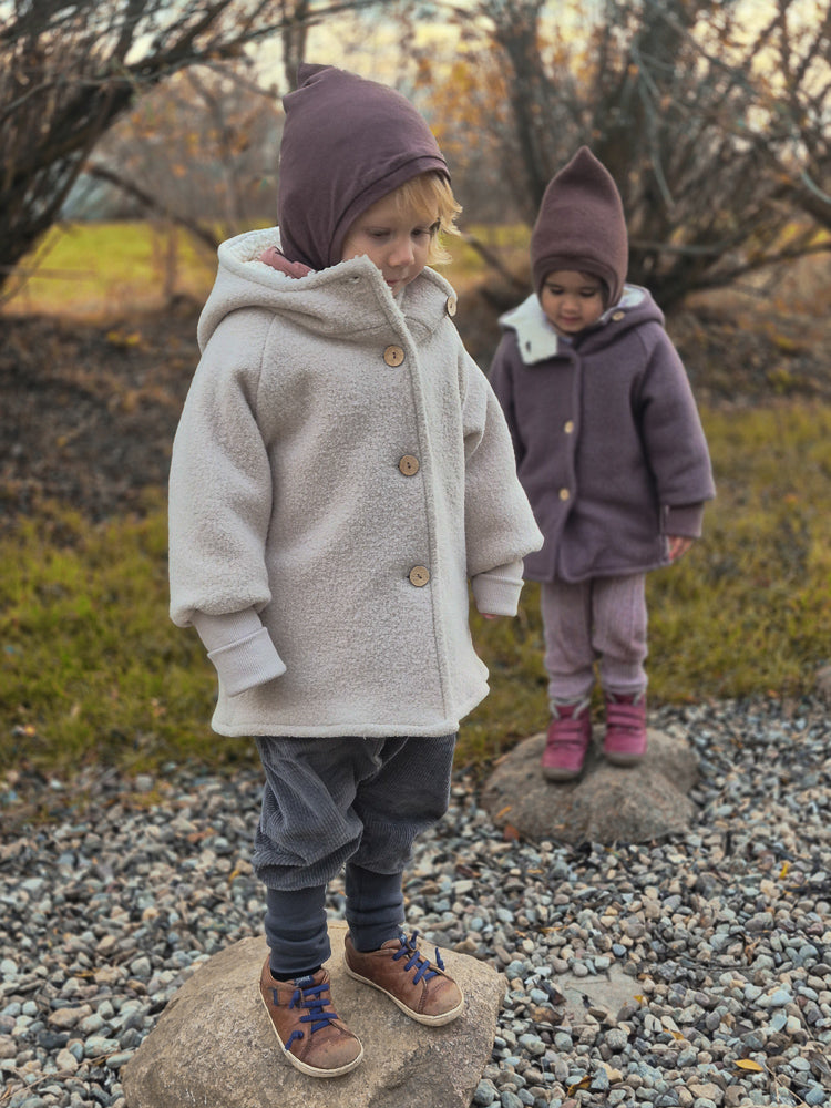 Zwei Kinder draußen; das vordere trägt eine Knickerbocker Breitcord Stretch - Maus, eine cremefarbene Fleecejacke, braunen Hut, Cordhose, hohe Socken, braune Schuhe. Ideal für kühle Herbsttage.