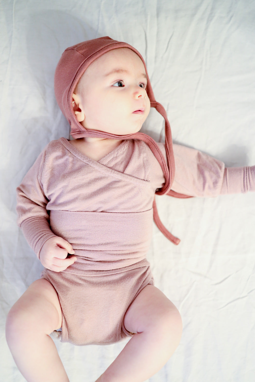 Babyhäubchen Kaschmir-Mix - Zimt: Ein Baby trägt eine weiche, elastische Mütze aus Kaschmir-Mix, ideal für Wärme und Schutz, auf einem Bett liegend. Baby Body für Erstausstattung Baby.