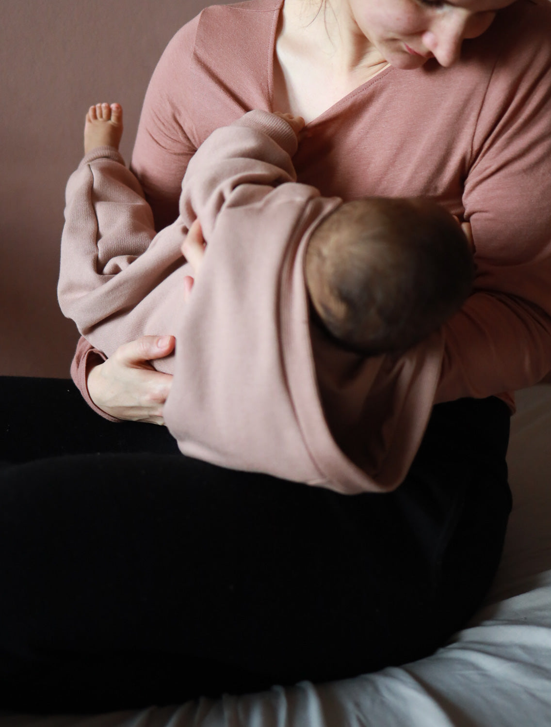 Frau hält Baby im Kuschelanzug Bio-Sweat - Puder, der bequem und atmungsaktiv ist. Der Overall hat krempelbare Bündchen und eine schräge Knopfleiste für einfaches Anziehen.