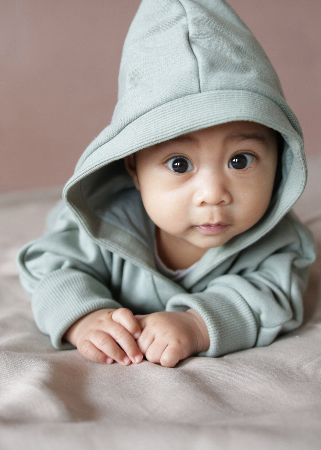 Kuschelanzug Bio-Sweat - Aqua: Ein Baby liegt auf dem Bauch und trägt einen kuscheligen Anzug mit Wichtelkapuze, ideal für drinnen und draußen.  Erstausstattung Baby und Baby Geschenk zur Geburt.
