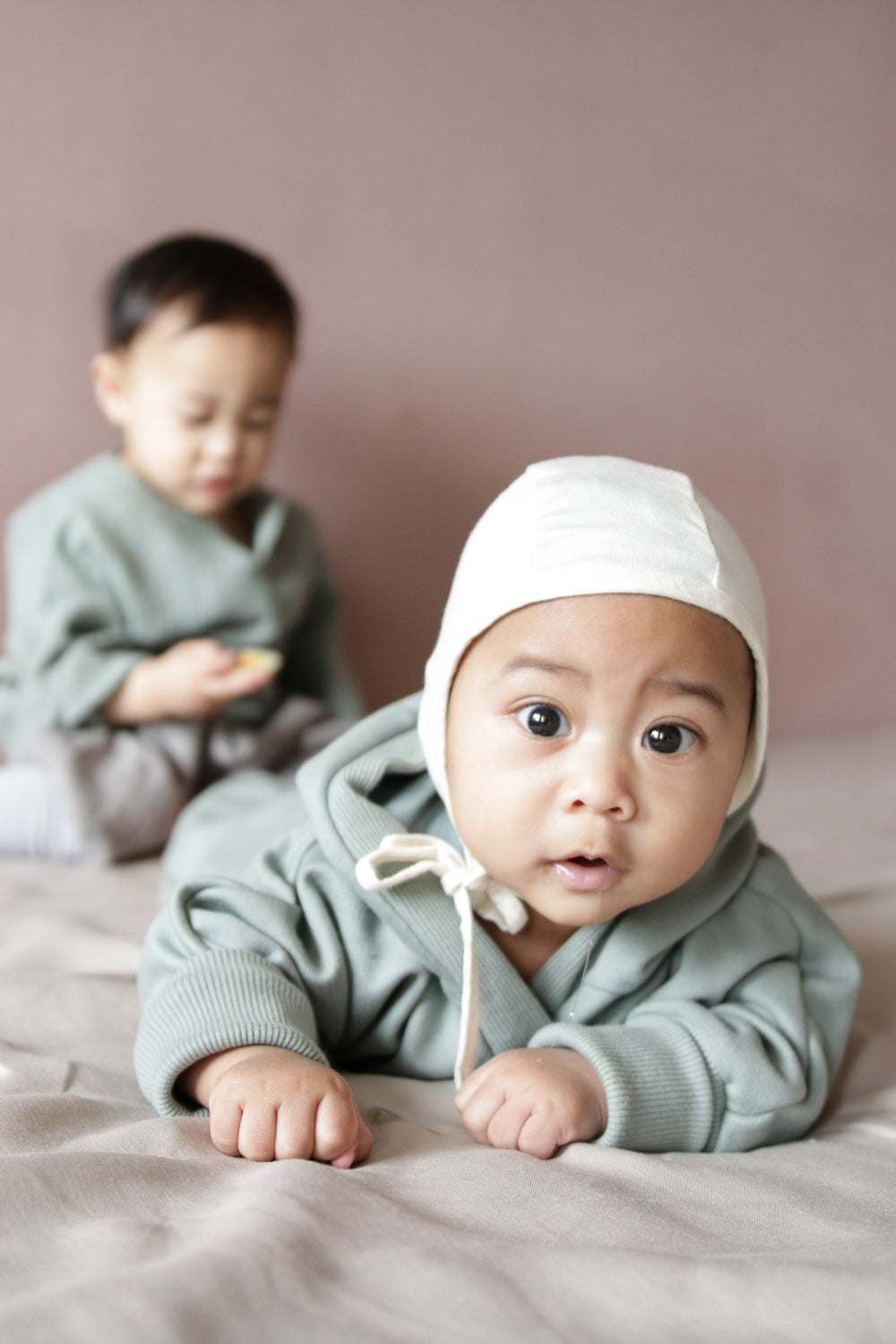 Baby auf einer Decke liegend, trägt den Kuschelanzug Bio-Sweat - Aqua mit Wichtelkapuze, aus weicher, angerauter Bio-Baumwolle, ideal für drinnen oder als wärmende Schicht an kälteren Tagen.  Erstausstattung Baby und Baby Geschenk zur Geburt.