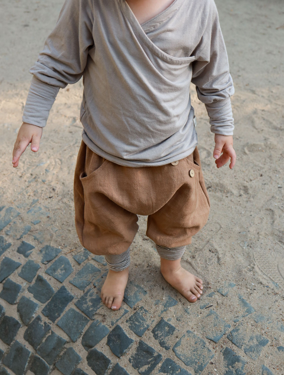 Ein Kind trägt Knickerbocker Leinen - Weizen, zeigt nur Beine und Füße. Die Hose besteht aus atmungsaktivem Leinen, hat elastische Bündchen und wächst mit, ideal für Sommer und Winter.