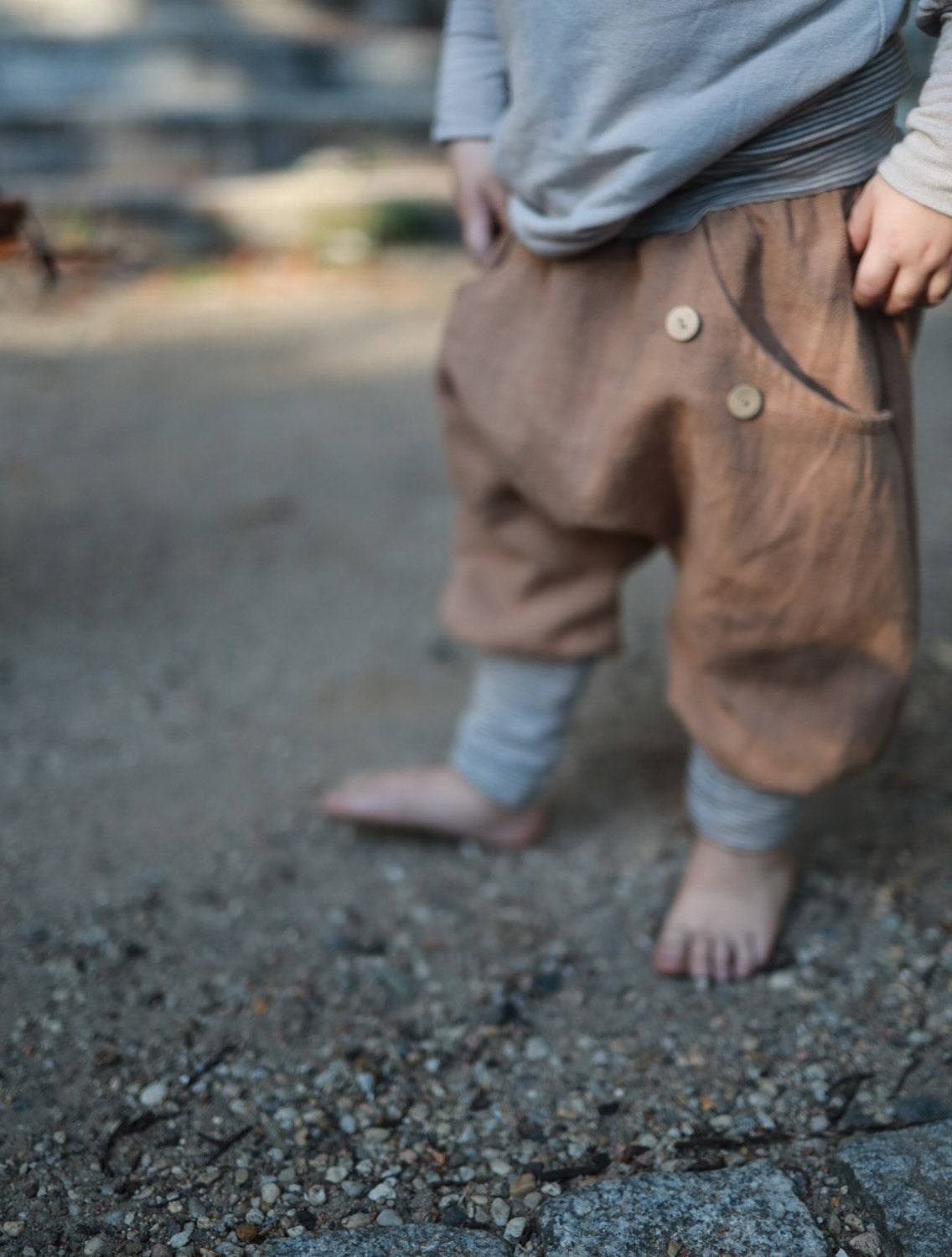 Ein Kind trägt Knickerbocker Leinen - Weizen, steht auf einem erdigen Untergrund. Die lockere Passform der Hose ist sichtbar, ideal für Komfort und Bewegungsfreiheit.