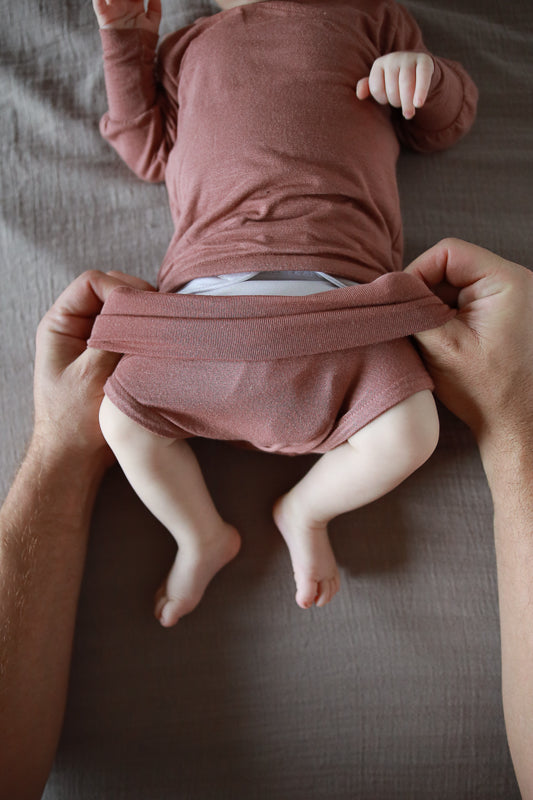 Vater zeiht dem Baby den mitwachsenden Babybody an