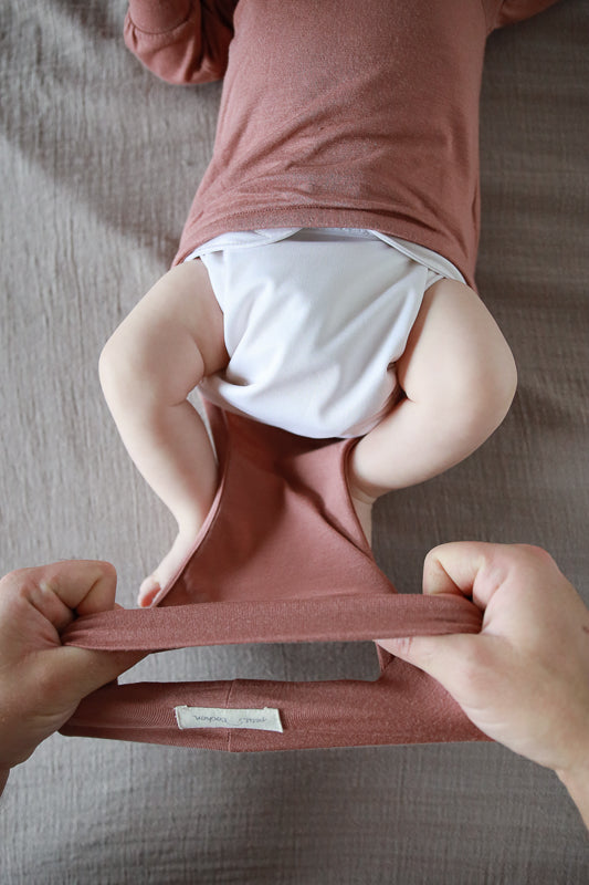 Vater zieht dem Baby den Loopbody in der Farbe Zimtan