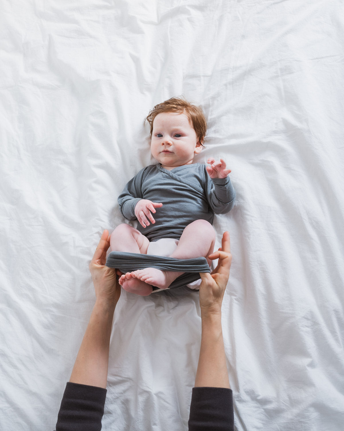 Mutter zieht Loop des mitachsenden Babybodys über die Beine des Babys