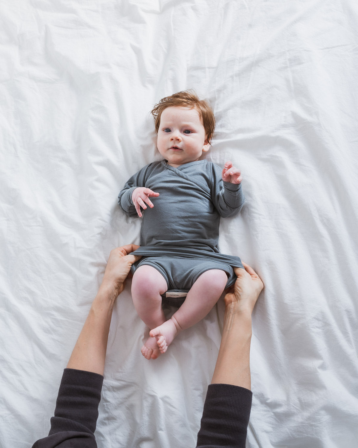 Mutter zieht dem Baby einen Loopbody in der Farbe Taube aus  Kaschmir-Mix an