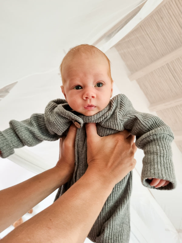 Eine Person hält ein Baby im Mini Overall Rippstrick - Maus, aus recycelter Baumwolle, mit Krempelbündchen und tiefem Schnitt für langes Mitwachsen.  Erstausstattung Baby und Baby Geschenk zur Geburt.