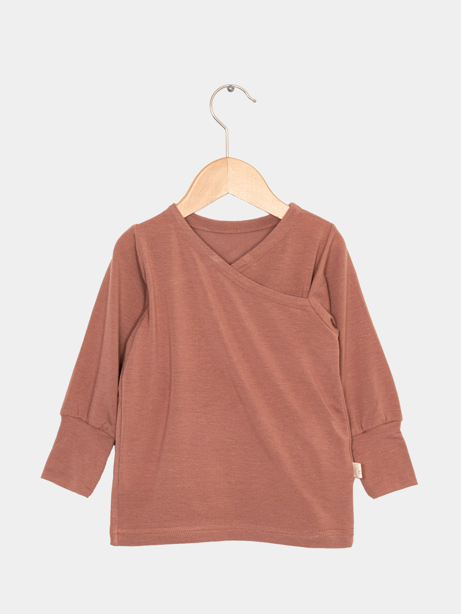 Wickelshirt aus Kaschmir-Mix - Zimt, präsentiert auf einem Holz-Schwinger. Kuschelweich, elastisch, atmungsaktiv, ideal als Shirt oder Unterhemd für Kinder.