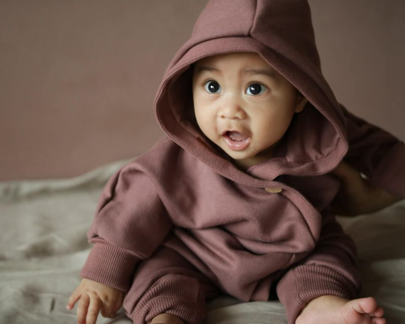Ein Baby trägt einen Baby Strampler, im Innenbereich. Es zeigt ein süßes Gesicht und gehört zur Babykleidungskategorie.
Baby Geschenke. 