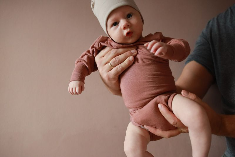 Eine Person hält ein Baby in einem zimtfarbenen Strampler. Der perfekte Baby body und die Erstausstattung für Babys.