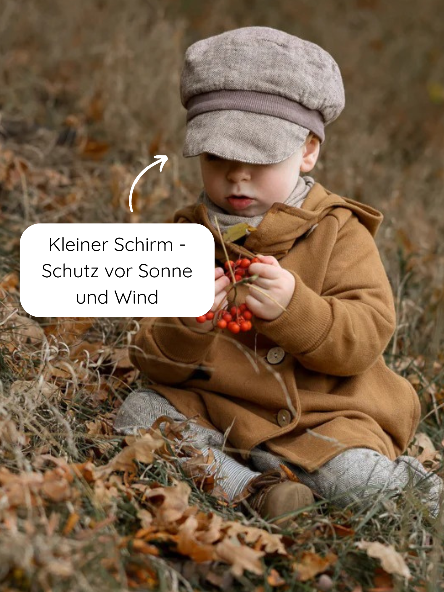 Kleinkind im Freien, trägt die Michelmütze Fischgrat Maus mit kleinem Schirm, hält rote Beeren. Die Mütze schützt vor Sonne und Wind und wächst dank Zugband mit.