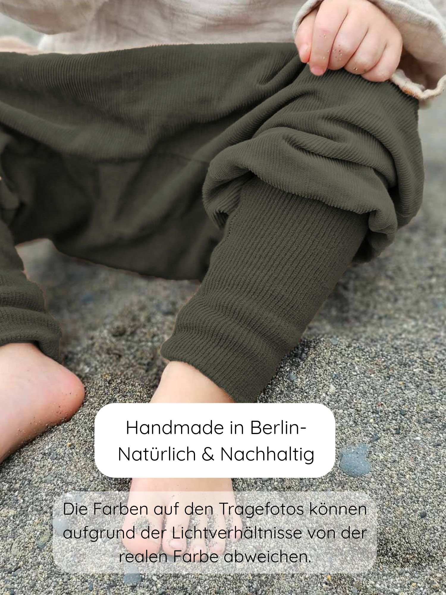 Kleinkind trägt Knickerbocker Feincord - Avocado, sitzt barfuß im Sand und zieht am elastischen Bund. Die olive-grünen, gerippten Hosen sind handgemacht in Berlin und bieten Bewegungsfreiheit für aktive Kinder.