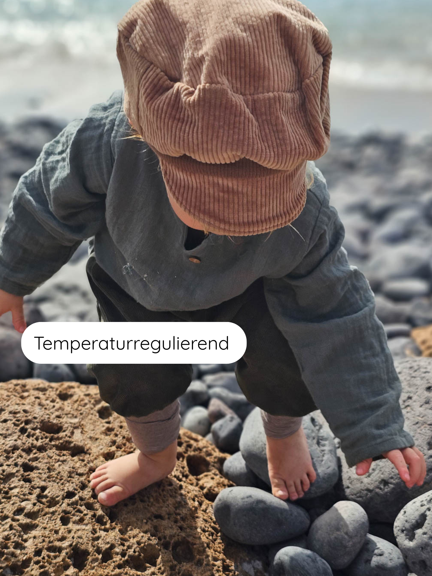 Kind mit Hemdchen Musselin - Eisblau am felsigen Ufer. Das luftige, ärmellose Kleidungsstück aus Bio-Musselin ist perfekt für warme Tage, bietet Bewegungsfreiheit und ist temperaturregulierend.