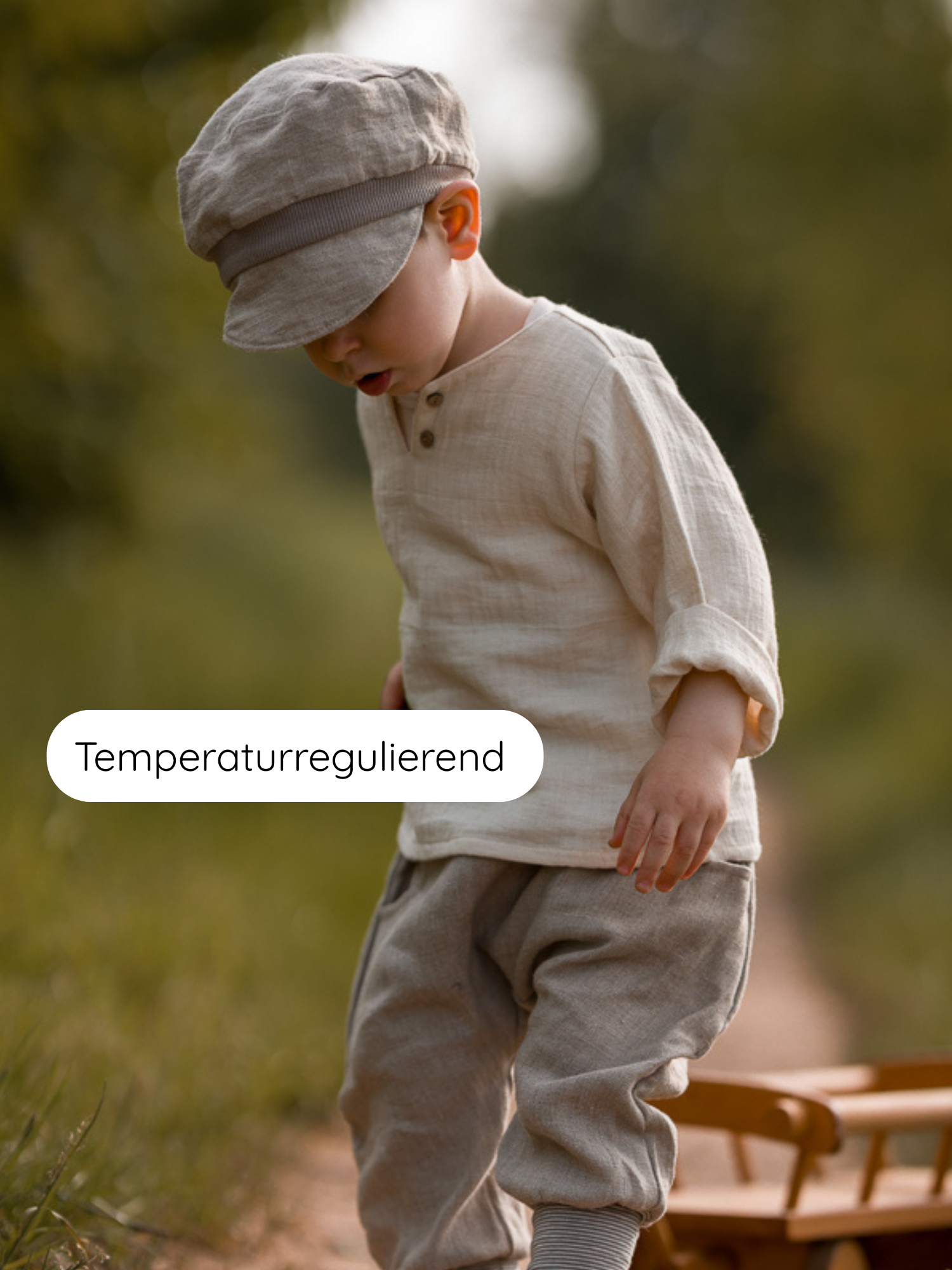 Kleinkind auf einem Pfad in Hemdchen Bio-Musselin - Natur, locker geschnitten, temperaturregulierend, neben einem Holzspielzeugwagen, ideal für warme Tage, atmungsaktiv und hautfreundlich.