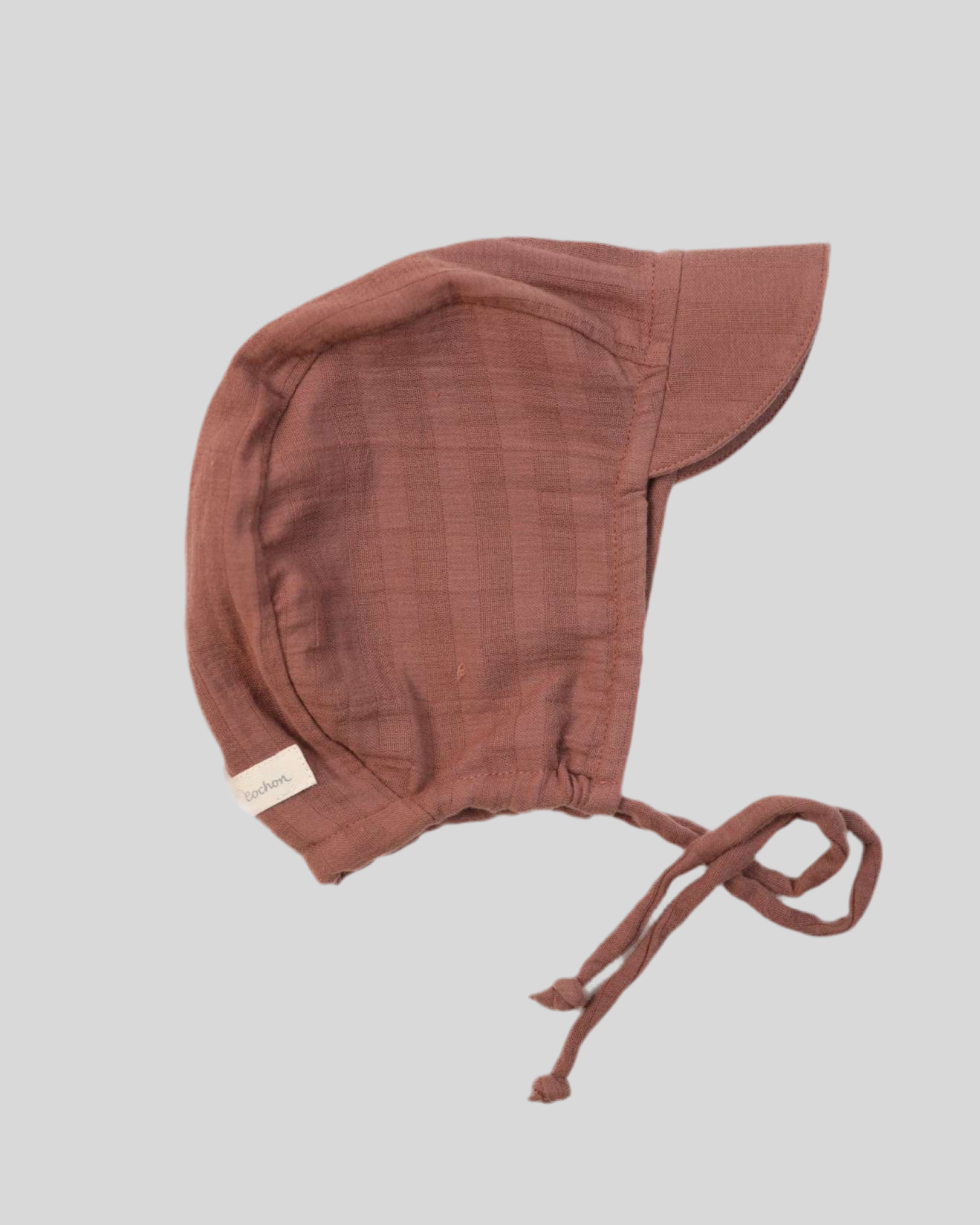 Baby Schirmmütze Bio-Musselin Zimt Gr.0M mit Kordel. Nahaufnahme zeigt braune Farbe, Stoffstruktur und weißen Etikett mit schwarzem Text. Perfekt für Neugeborene, modisch und funktionell.