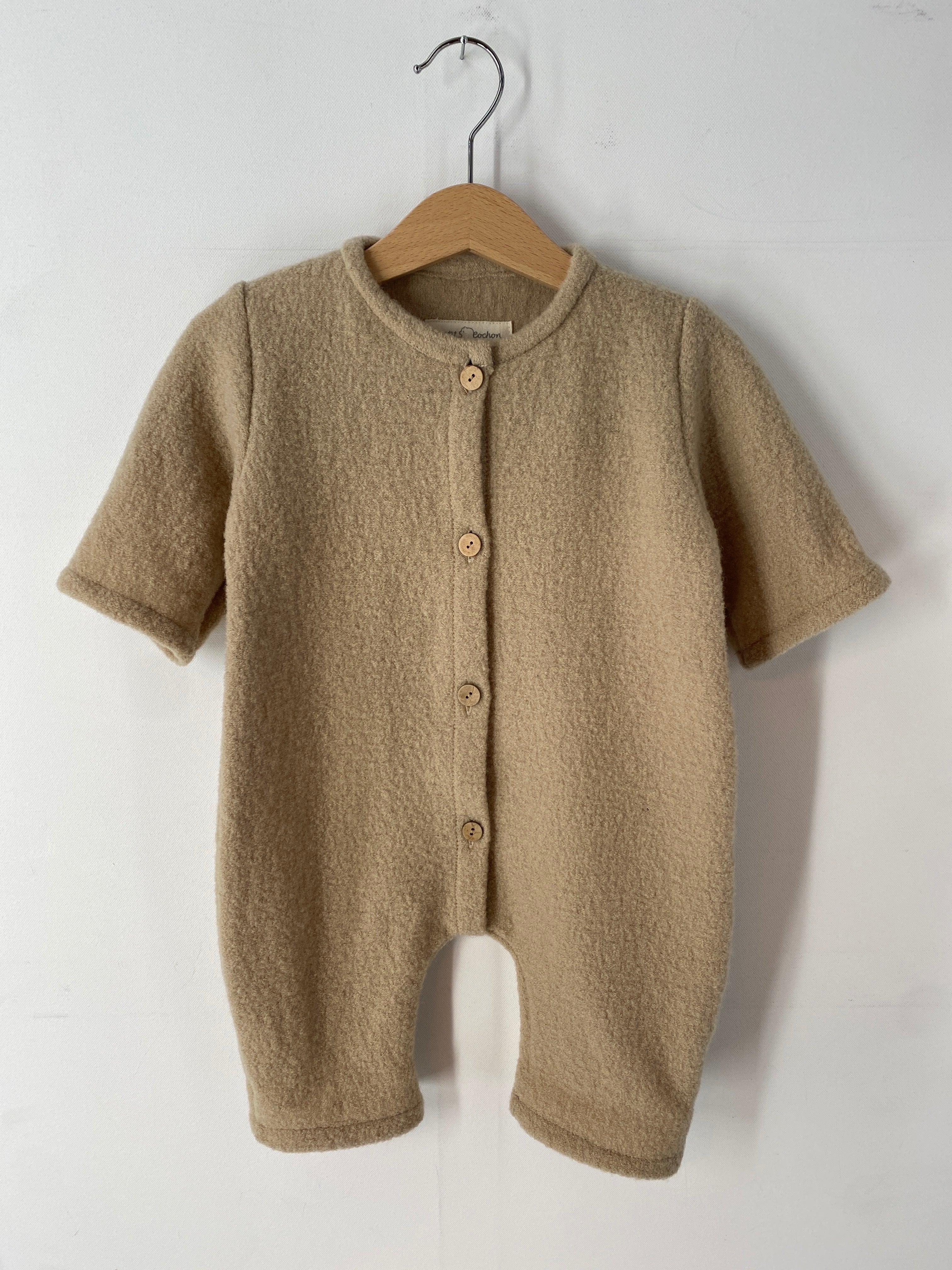 NEU Overall Wollwalk Creme Gr 3M auf einem Holzkleiderbügel an einem Schwinger, mit sichtbaren Knöpfen und Details des ungefütterten Stoffes, dargestellt in einer Nahaufnahme.