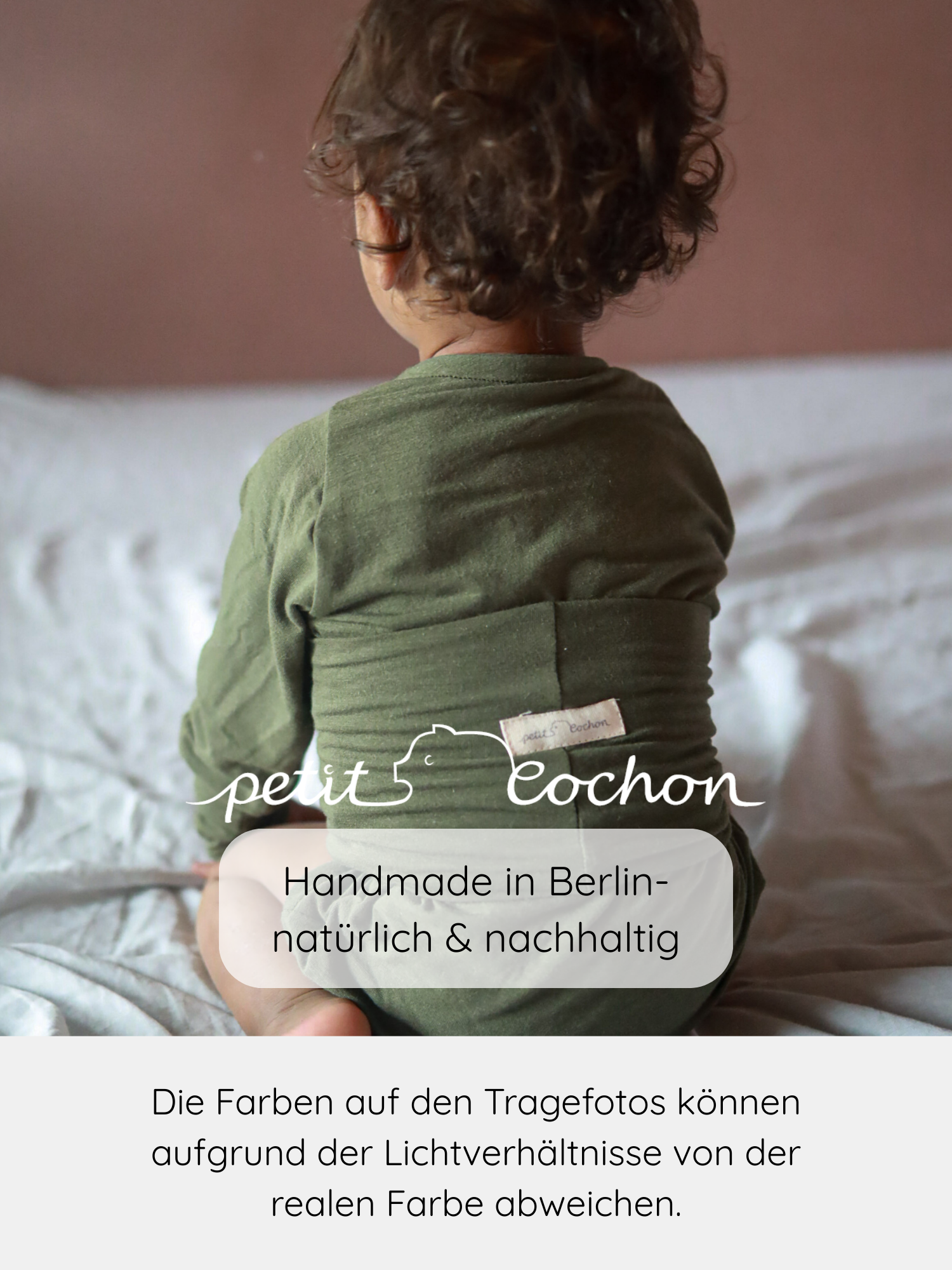 Ein Kind sitzt auf einer weichen Unterlage, eingehüllt in ein olivgrünes Tragetuch. Der Loopbody Kaschmir-Mix - Pistazie von petit Cochon bietet Komfort und wächst mit, aus nachhaltigem Kaschmir-Mix.