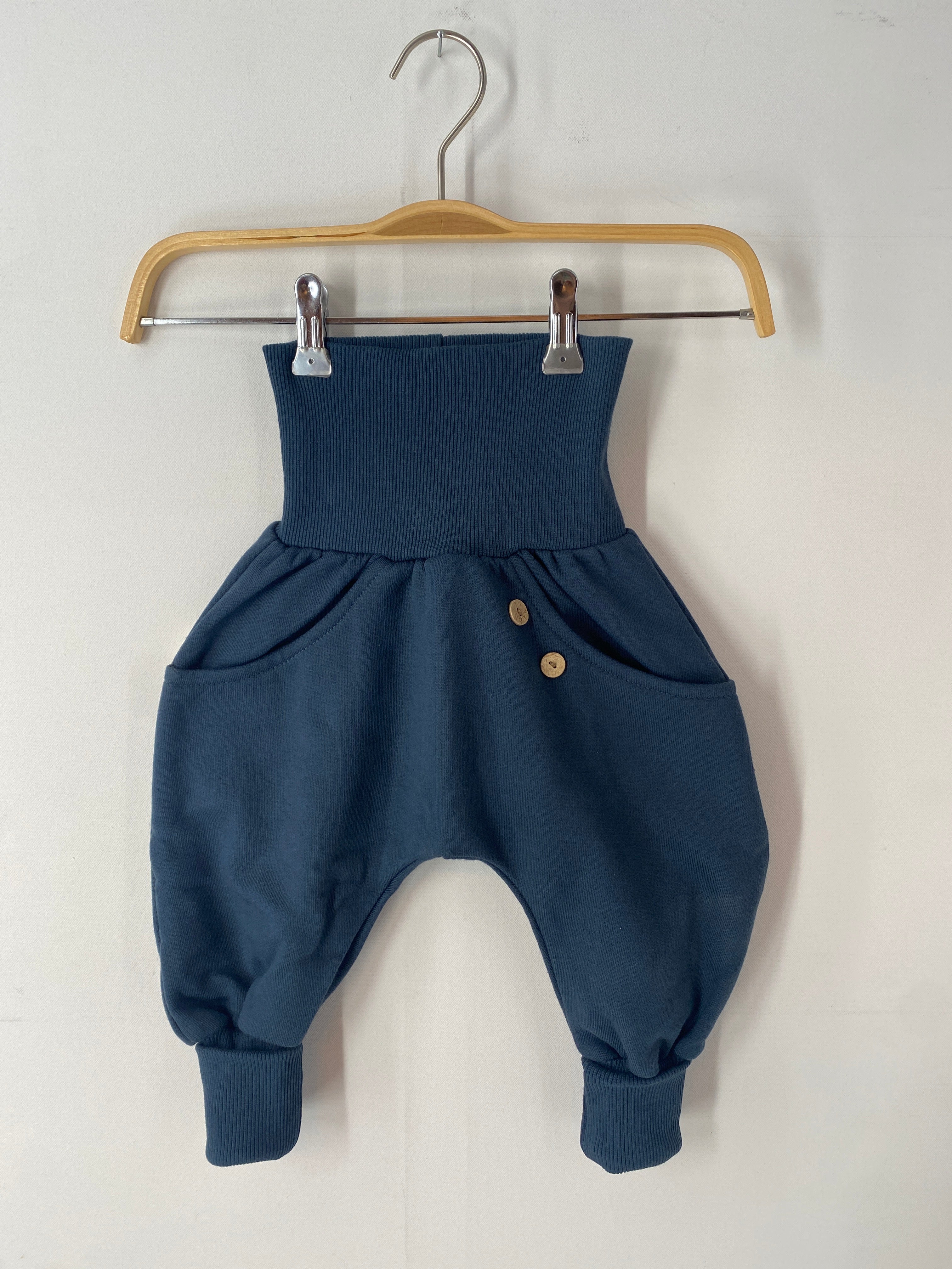 Ein blauer Knickerbocker-Bio-Sweat-Marine-Größe 2Y, neu, auf einem Kleiderbügel mit sichtbaren Knöpfen und geschwungenen Nähten, präsentiert auf einem Holzgestell.