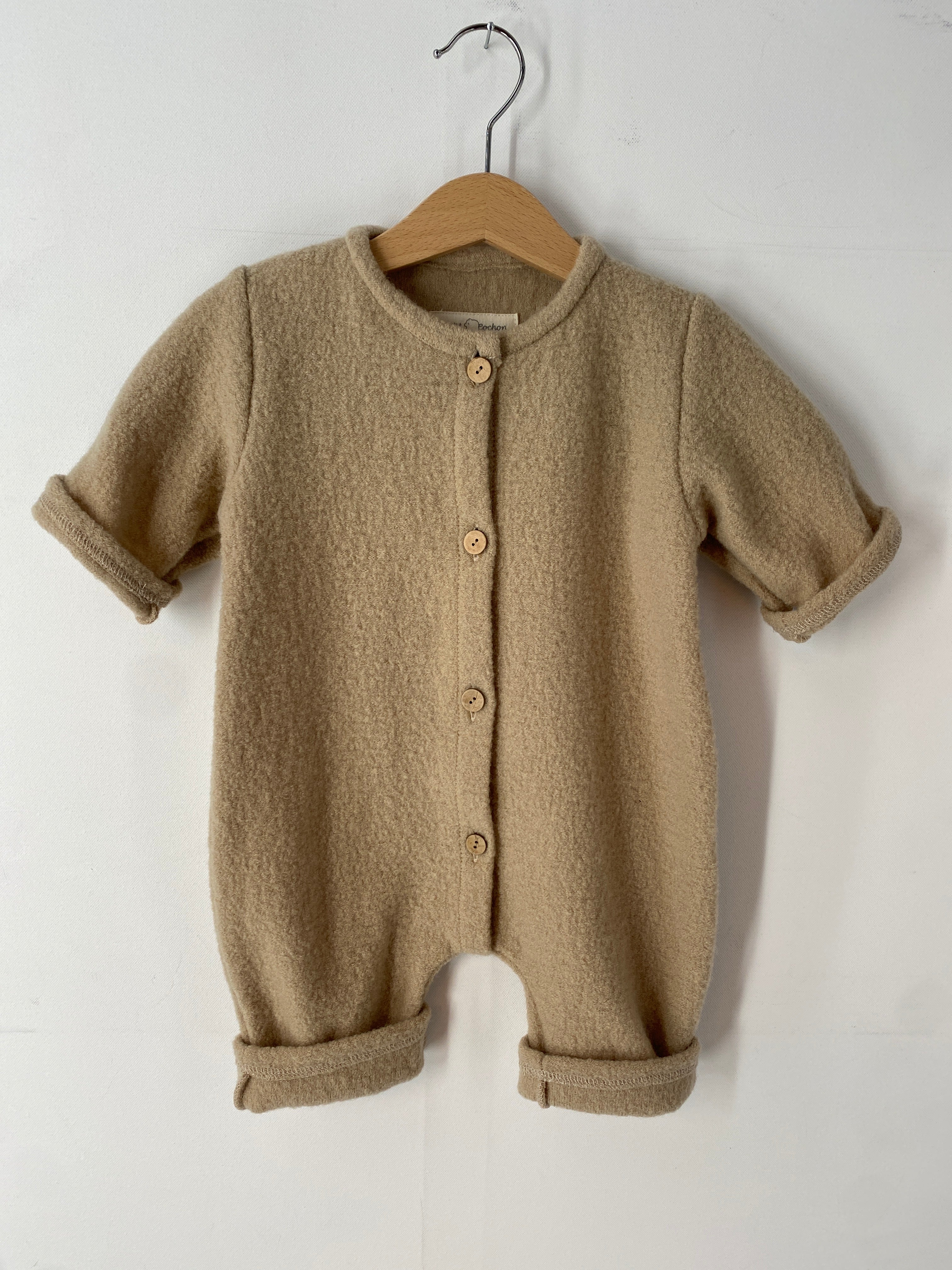 NEU Overall Wollwalk Creme Gr 3M hängt auf einem Schwinger, zeigt einen gestrickten Stoff mit Knöpfen, ungefüttert, ideal für Babys in kühleren Monaten.