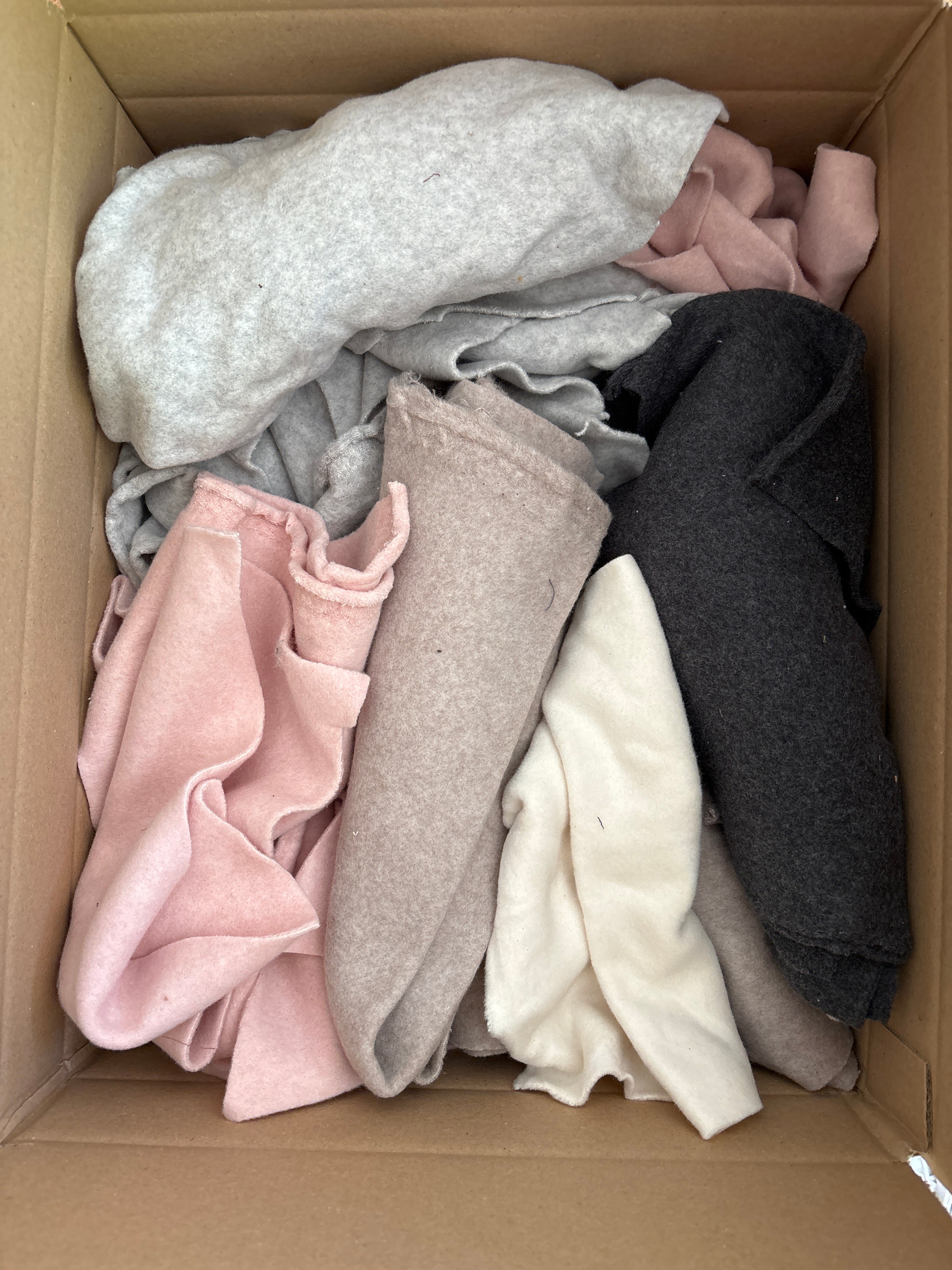 Ca. 3,5 kg Stoffreste Bio-Baumwoll-Plüsch im Karton, bestehend aus verschiedenen Stoffstücken und Mustern, einschließlich schwarzem und weißem Plüsch sowie rosa und grauen Decken, ideal zum Nähen und Basteln.