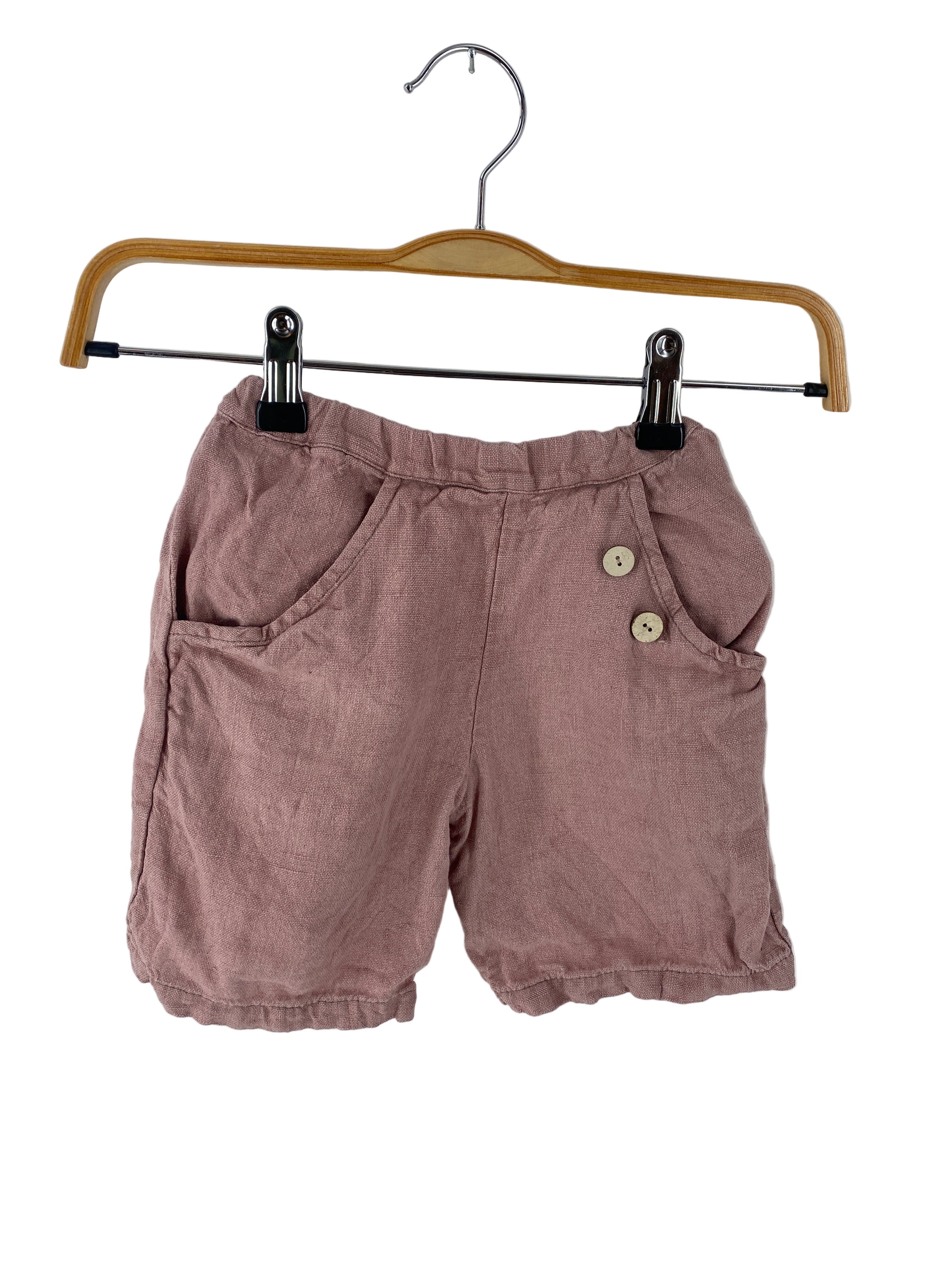 Kopie Kurze Buxe Leinen Rosé Gr 2Y: Staubrosa Leinen-Mischung Shorts mit elastischem Bund, zwei Fronttaschen, verziert mit zwei kleinen holzartigen Knöpfen, auf einem Holzbügel mit Metallclips präsentiert, Zustand: gut.