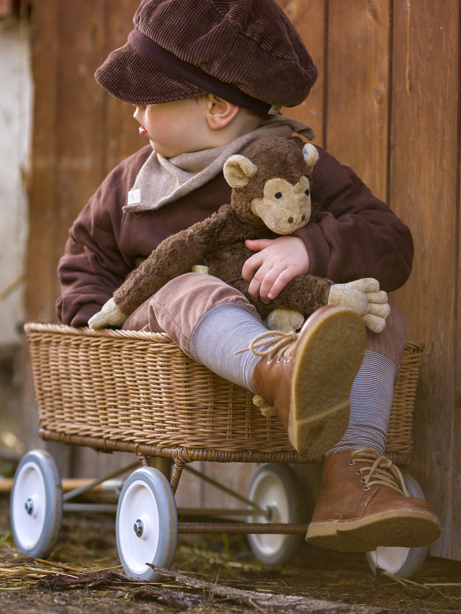 Kleinkind trägt Pulli Bio-Sweat - Schoko und sitzt im Korbwagon. Der Pulli aus Bio-Sweat bietet Komfort und Bewegungsfreiheit, ideal für Alltag und Spiel. Kombiniert mit Strumpfhose und Stiefeln.
