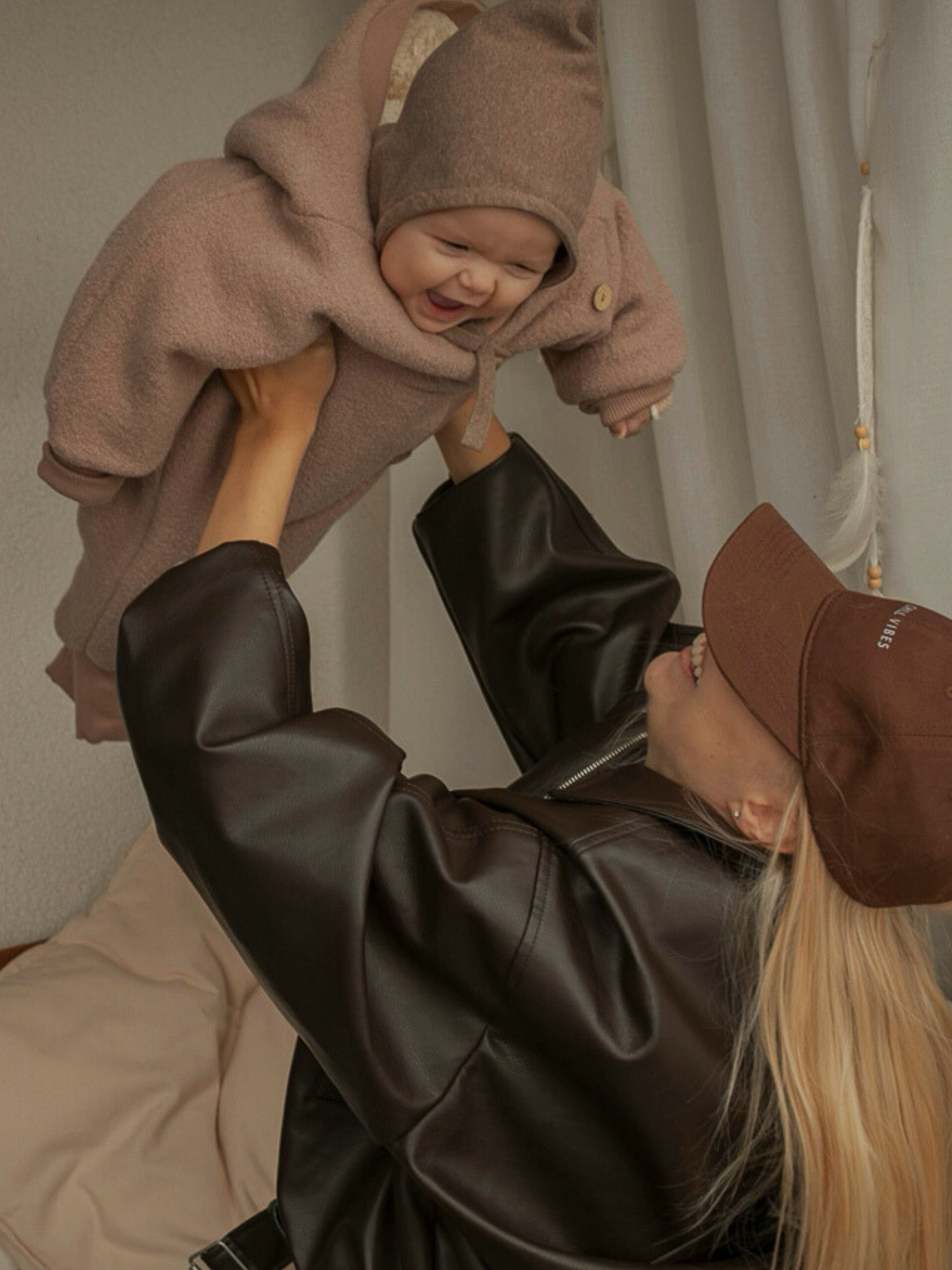 Ein Erwachsener hält ein lachendes Baby im Winter Wollwalk Overall mit Teddyfutter- Puder, das in einem weichen, hellbraunen, kapuzenartigen Outfit gebündelt ist, hoch.