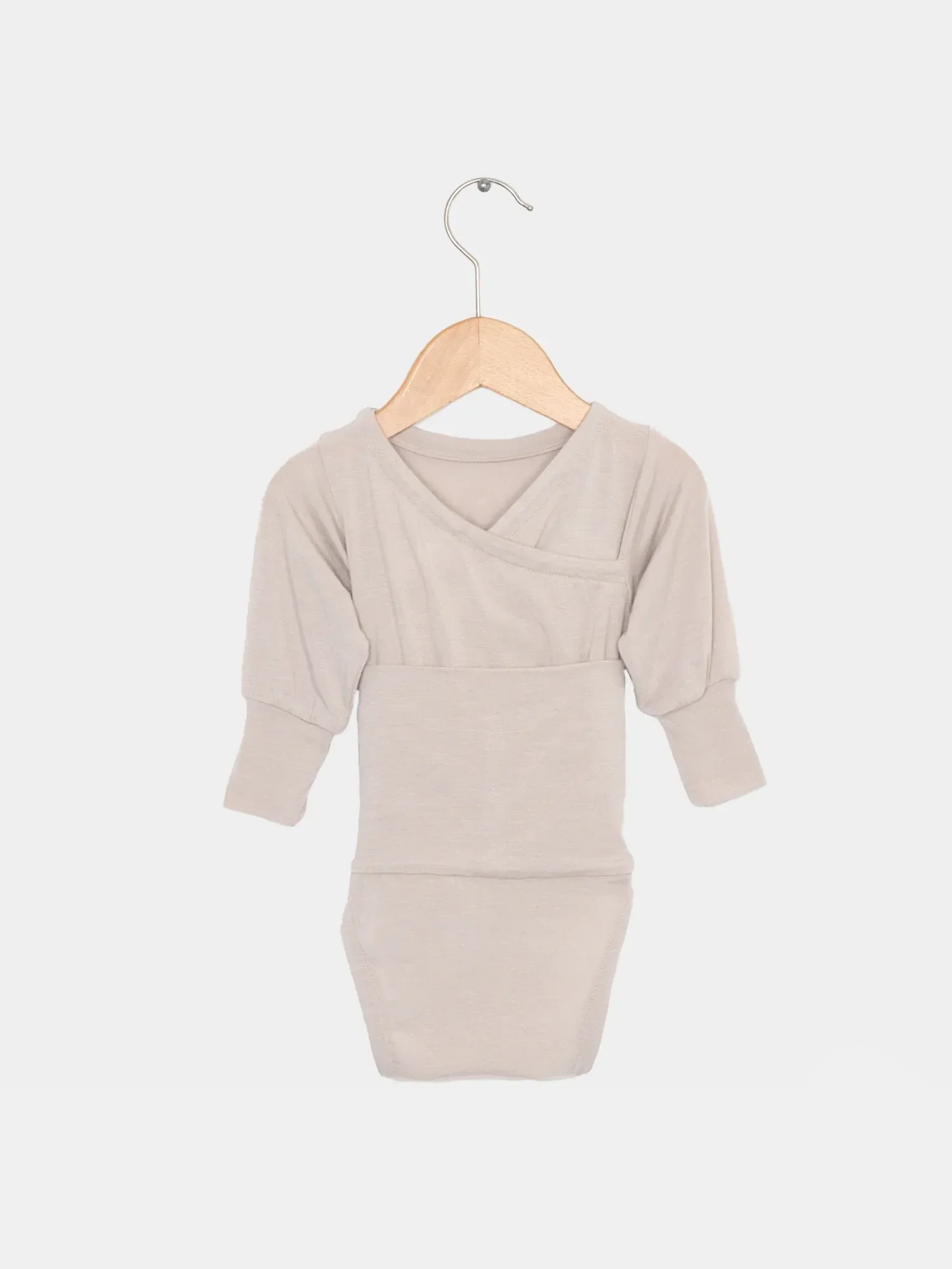 Loopbody Kaschmir-Mix - Sand: Ein langärmliger, sandfarbener Baby-Body mit kimonoartigem Wickelstil, aus Kaschmir-Mix, auf einem Holzkleiderbügel präsentiert, zeigt Eleganz und kuschelige Weichheit.