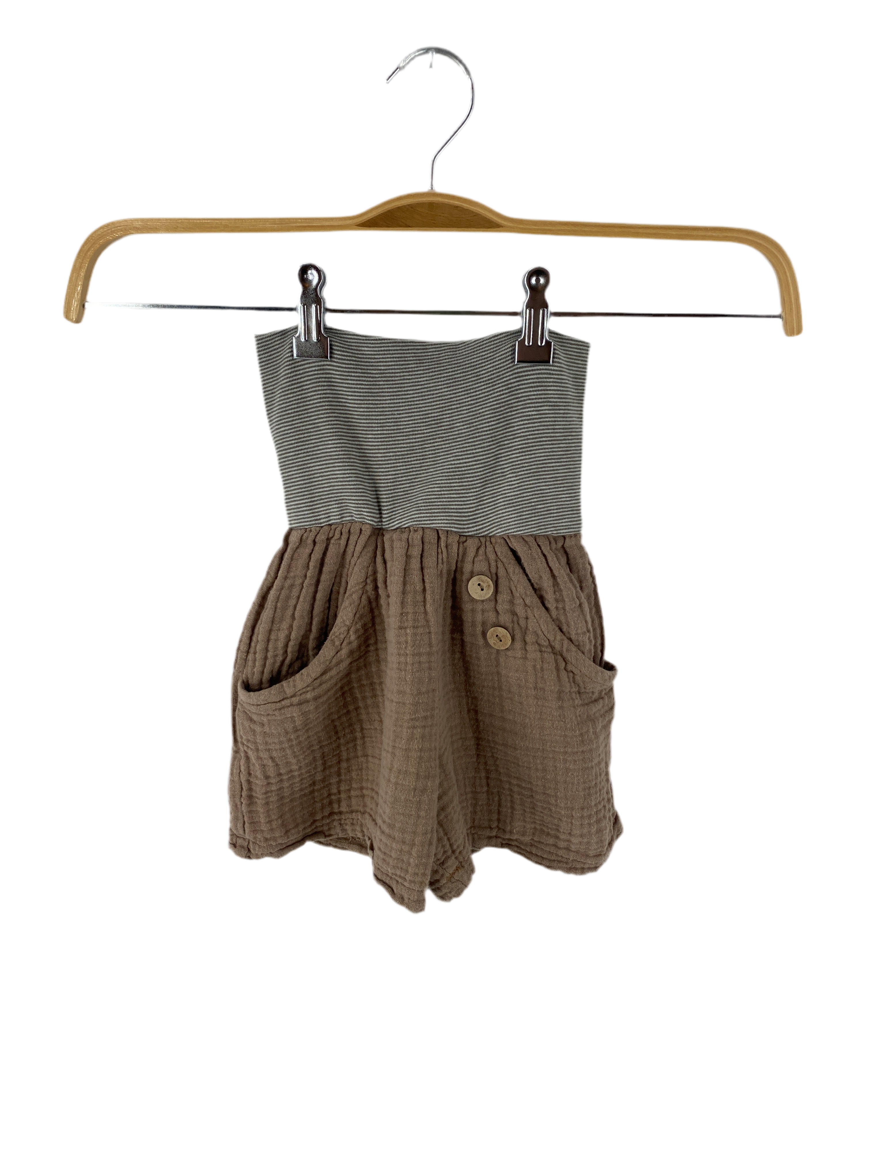 Kurze Buxe Musselin Praline Gr 2/3Y: Kinder-Strapless-Romper mit grauem Streifenbund und crinkle-light-braunem Unterteil, zwei Fronttaschen und dekorativen Holzknöpfen, auf Holzkleiderbügel präsentiert. Zustand: gut.
