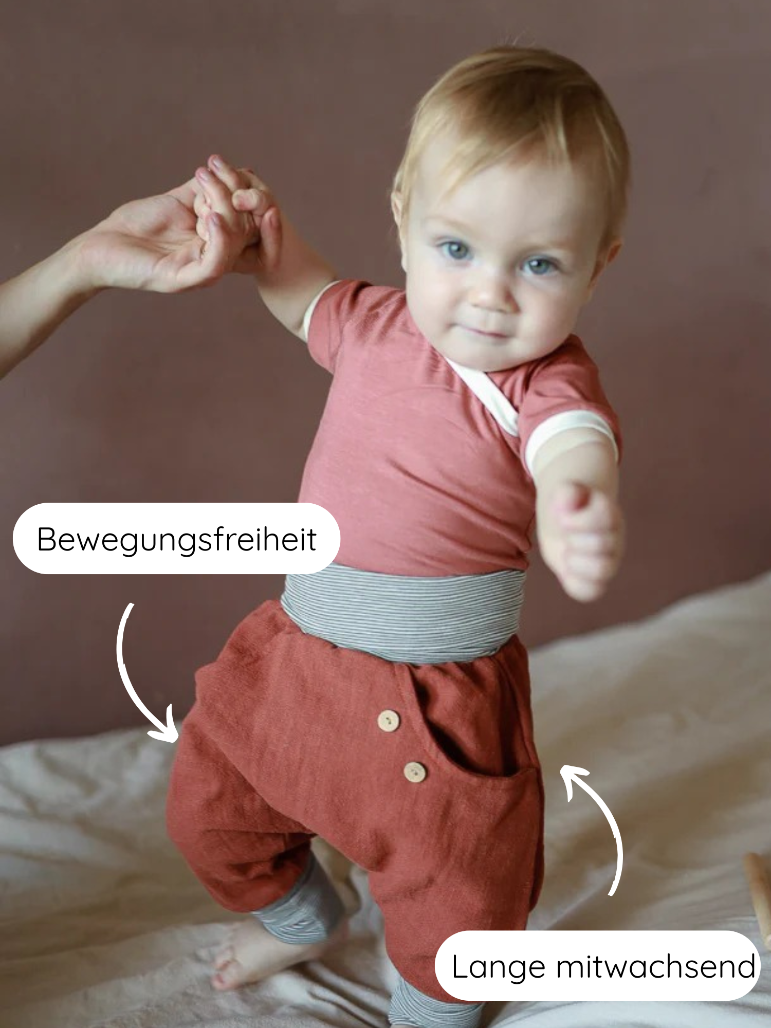 Kleinkind lernt laufen, trägt Knickerbocker Leinen - Terracotta mit breitem, gestreiftem Bündchen. Hervorgehobene Merkmale: Bewegungsfreiheit und mitwachsend. Perfekt für Komfort und Langlebigkeit.