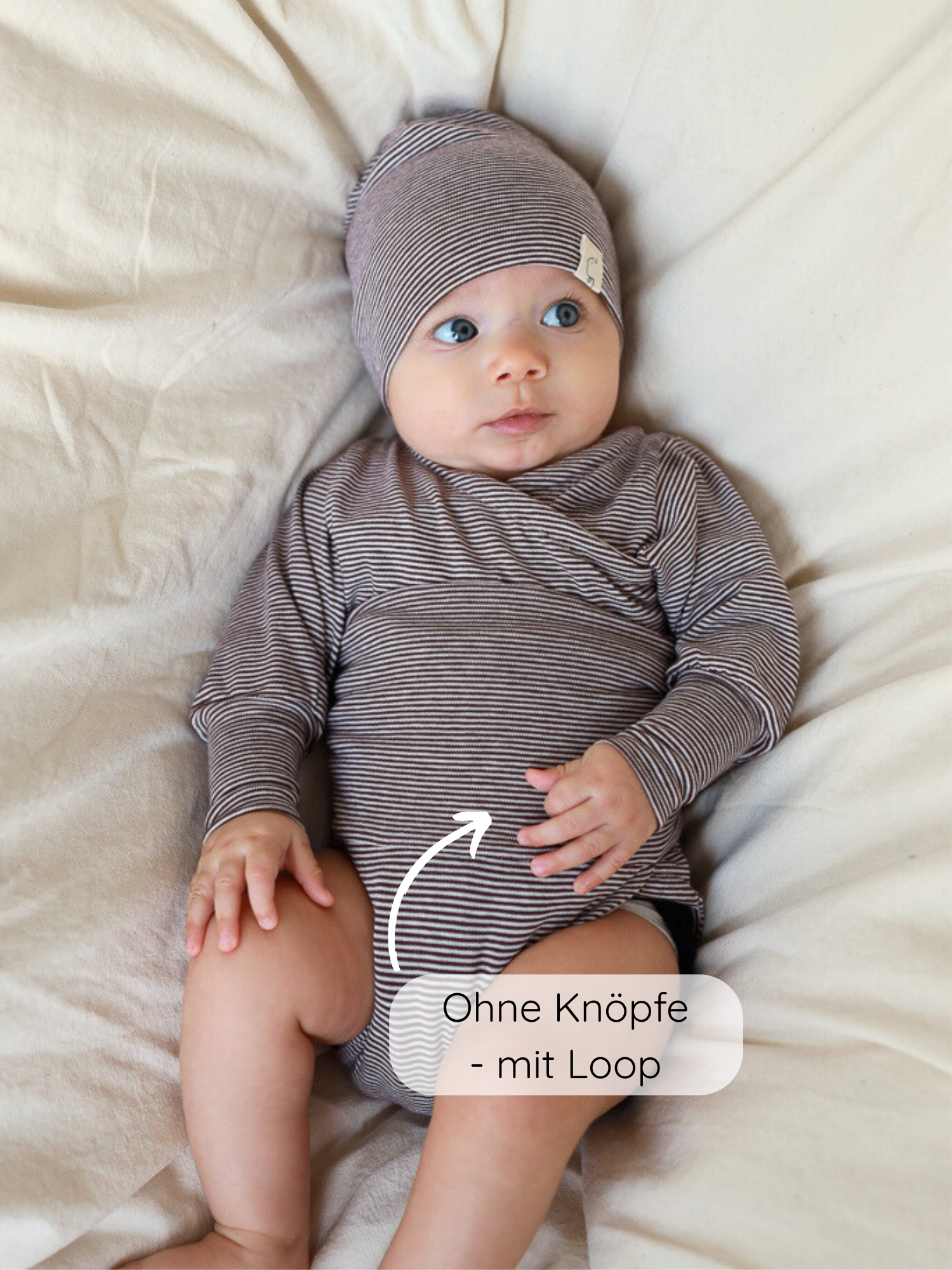Baby in einem Loopbody Bio-Baumwolle-Ringel Schoko liegt auf weichem Untergrund. Bodysuit ohne Knöpfe, mit Loop, wächst bis zu einem Jahr mit. Beanie passend zum Bodysuit.